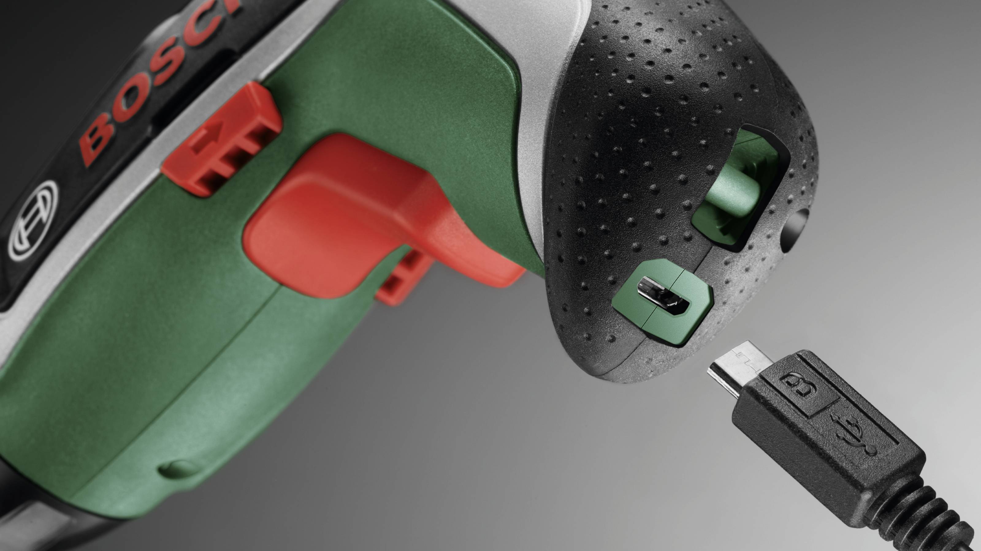 Akkuschrauber in Nahaufnahme mit Blick auf das Ladeanschluss, daneben ein passendes USB-Kabel zum Aufladen.