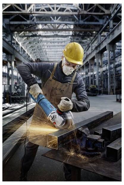 Ein Arbeiter in einer Fabrik schleift einen Stahlträger mit einem Elektrowerkzeug, wobei Funken sprühen. Er trägt Sicherheitsausrüstung, einschließlich Handschuhe, Schutzbrille und Helm.