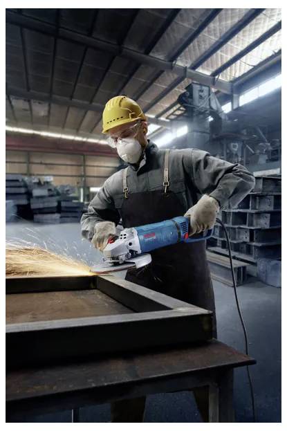 Ein Arbeiter in Schutzausrüstung verwendet einen Winkelschleifer und erzeugt Funken in einer industriellen Werkstattumgebung.