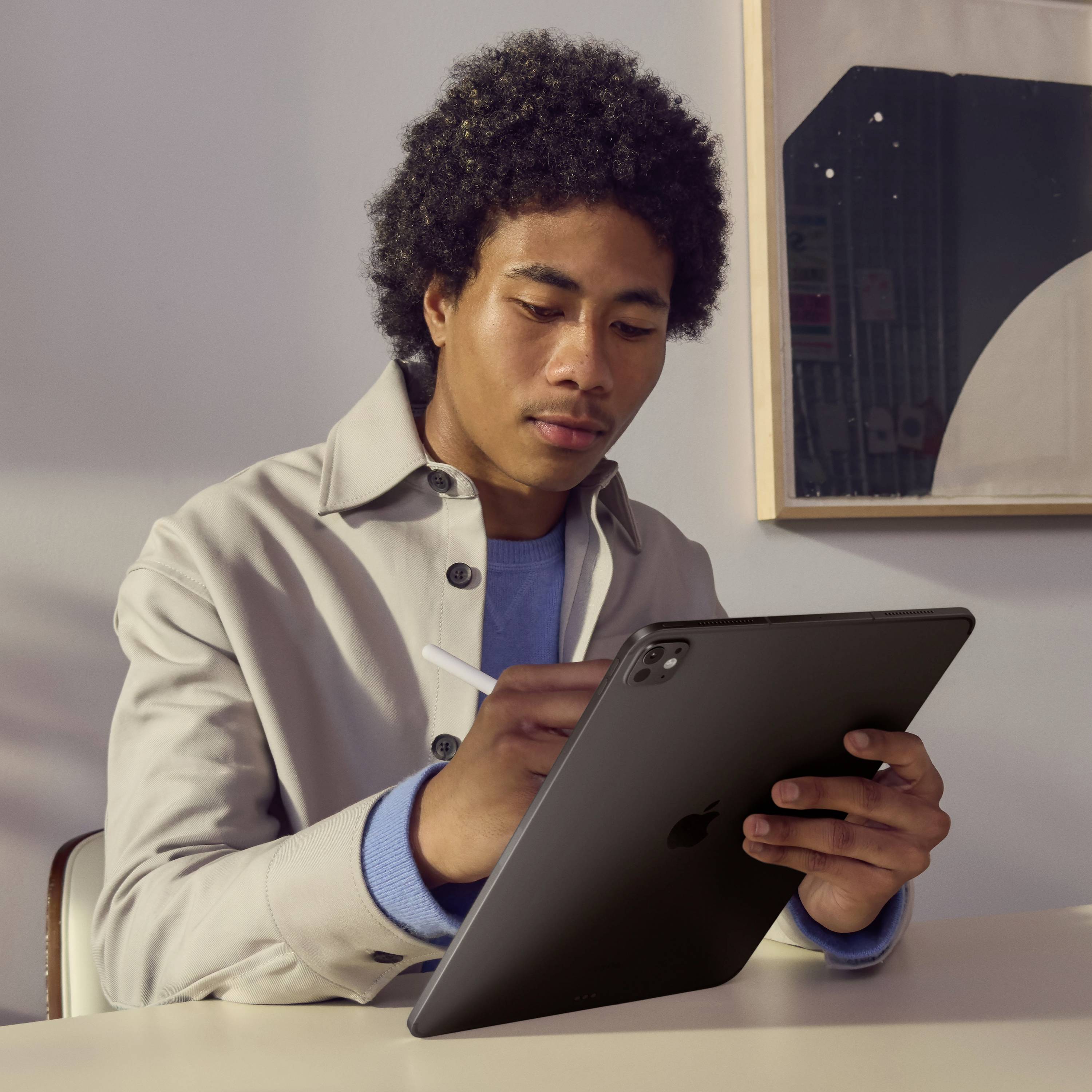 Eine Person sitzt und hält ein Tablet, konzentriert schauend, mit einem Stift in der Hand. Im Hintergrund sind verschwommene Formen zu sehen.