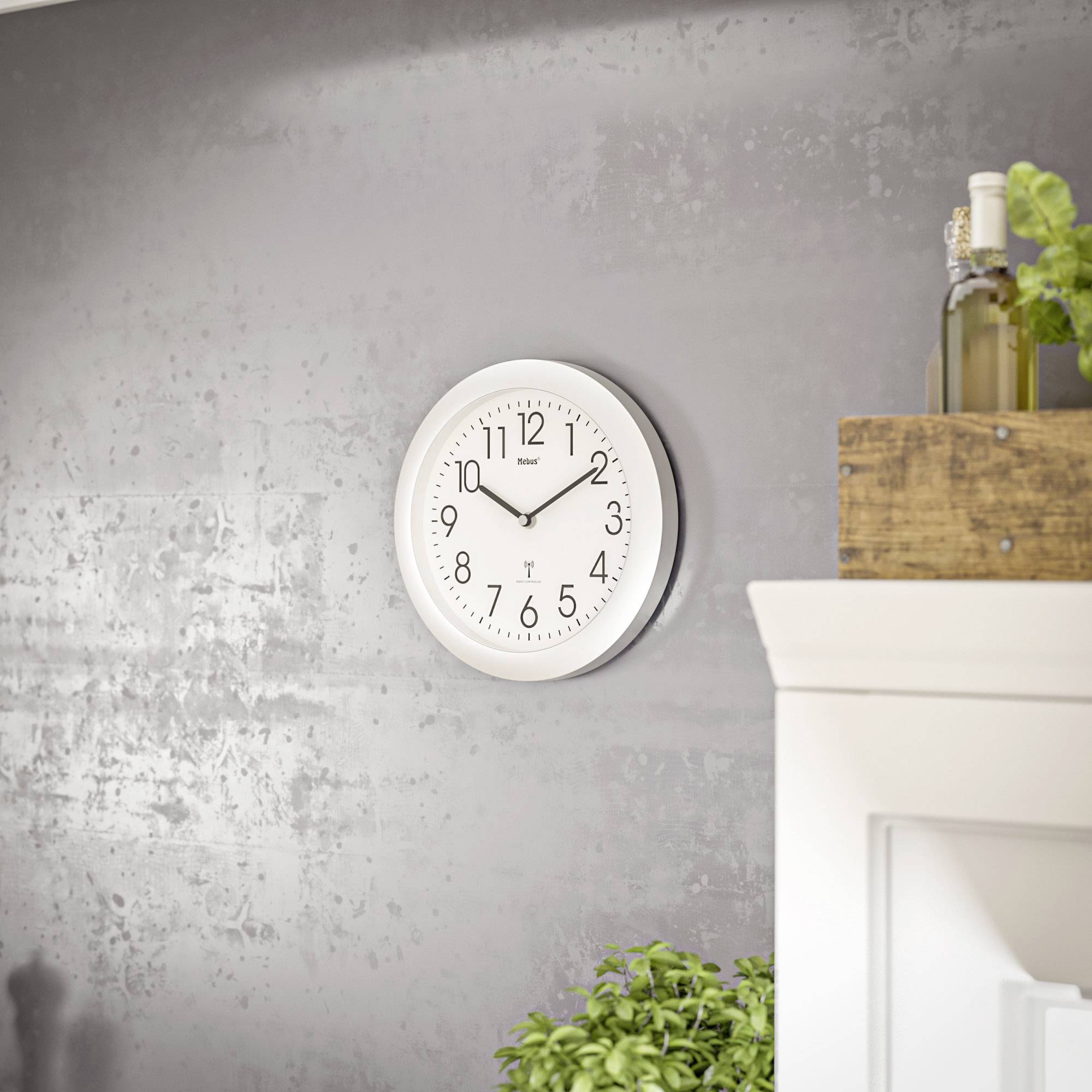 Eine weiße Wanduhr zeigt 10:10. In der Nähe befinden sich Holzkisten mit Pflanzen auf einem weißen Schrank. Die Umgebung ist modern und minimalistisch.