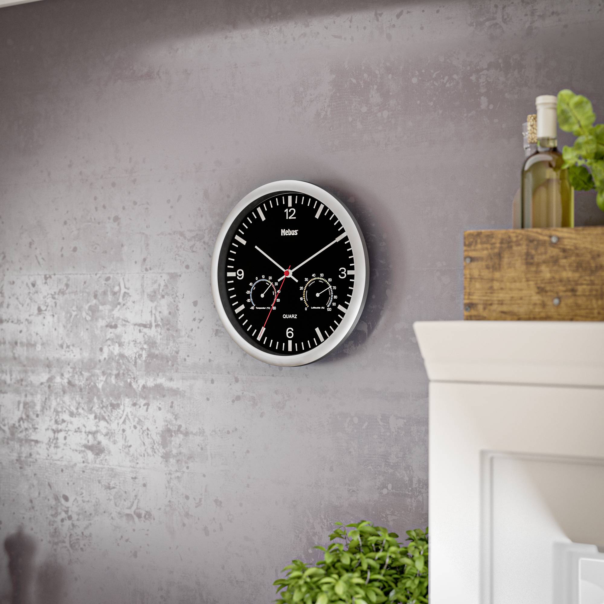 Eine runde Wanduhr mit schwarzem Zifferblatt und weißen Zahlen zeigt die Uhrzeit 10:09 an. Links unten ist eine Pflanze sichtbar.