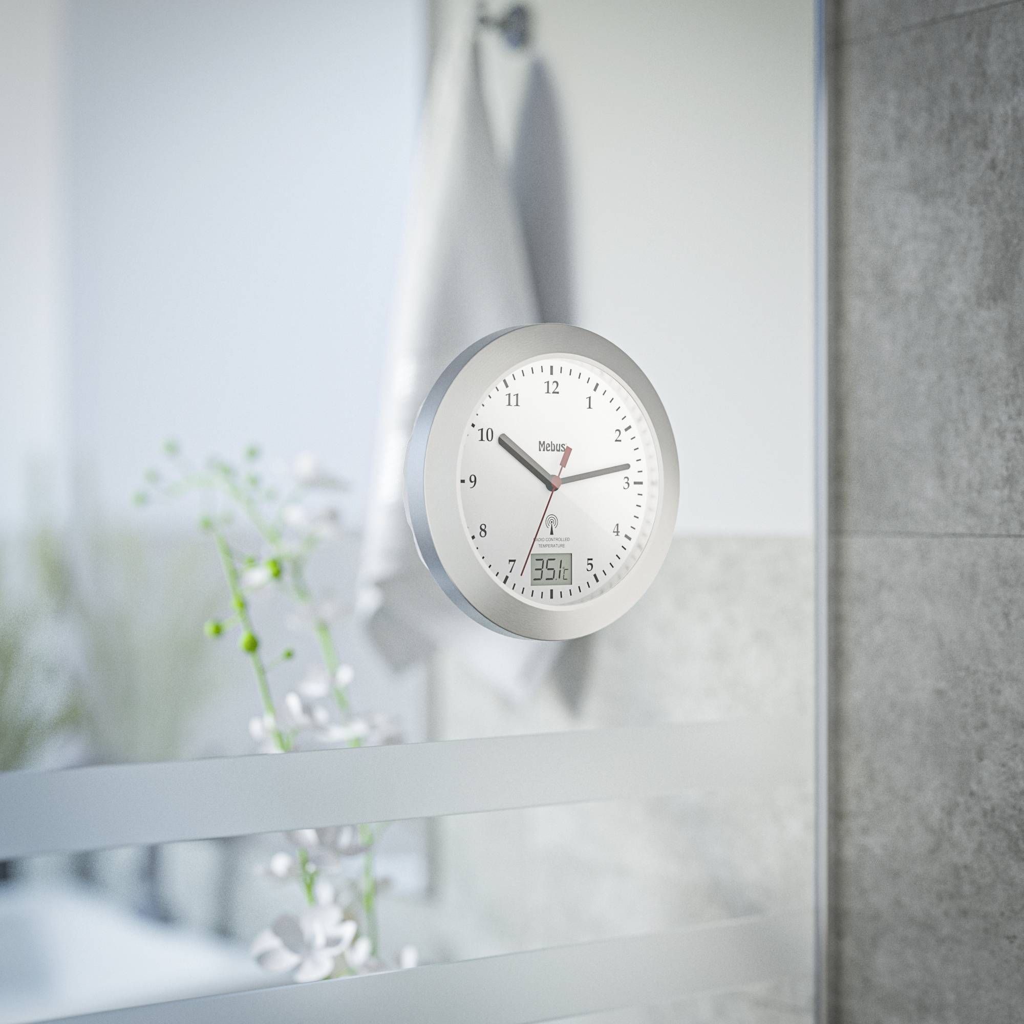 Eine silberne Wanduhr zeigt 11:07 Uhr an. Im Hintergrund sind unscharf Pflanzendekorationen und ein Handtuch zu sehen.