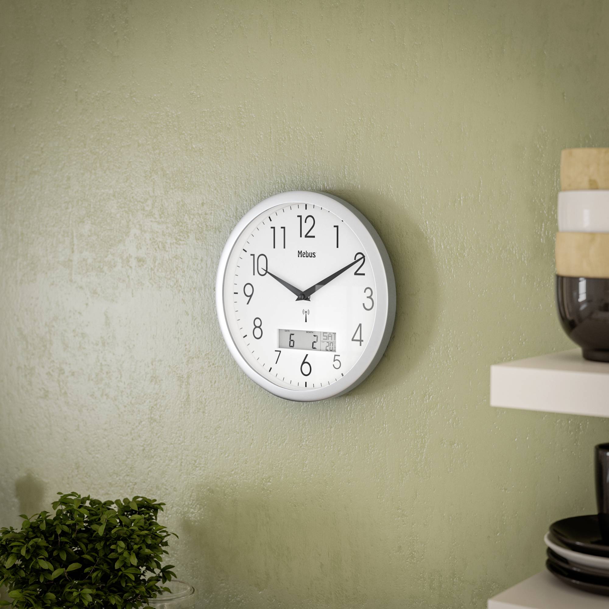 Eine analoge Wanduhr mit weißen Hintergrund und schwarzen Ziffern, zeigt 10:09 Uhr. Im Vordergrund sind Pflanze und Vase sichtbar.