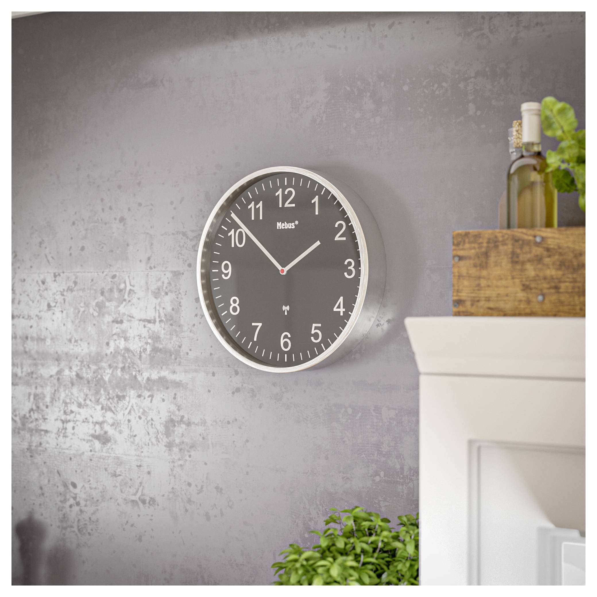 Eine graue Wanduhr mit weißen Ziffern und Zeigern ist an einer strukturierten grauen Wand angebracht, wobei eine Pflanze und Flaschen auf einem nahegelegenen Regal sichtbar sind.