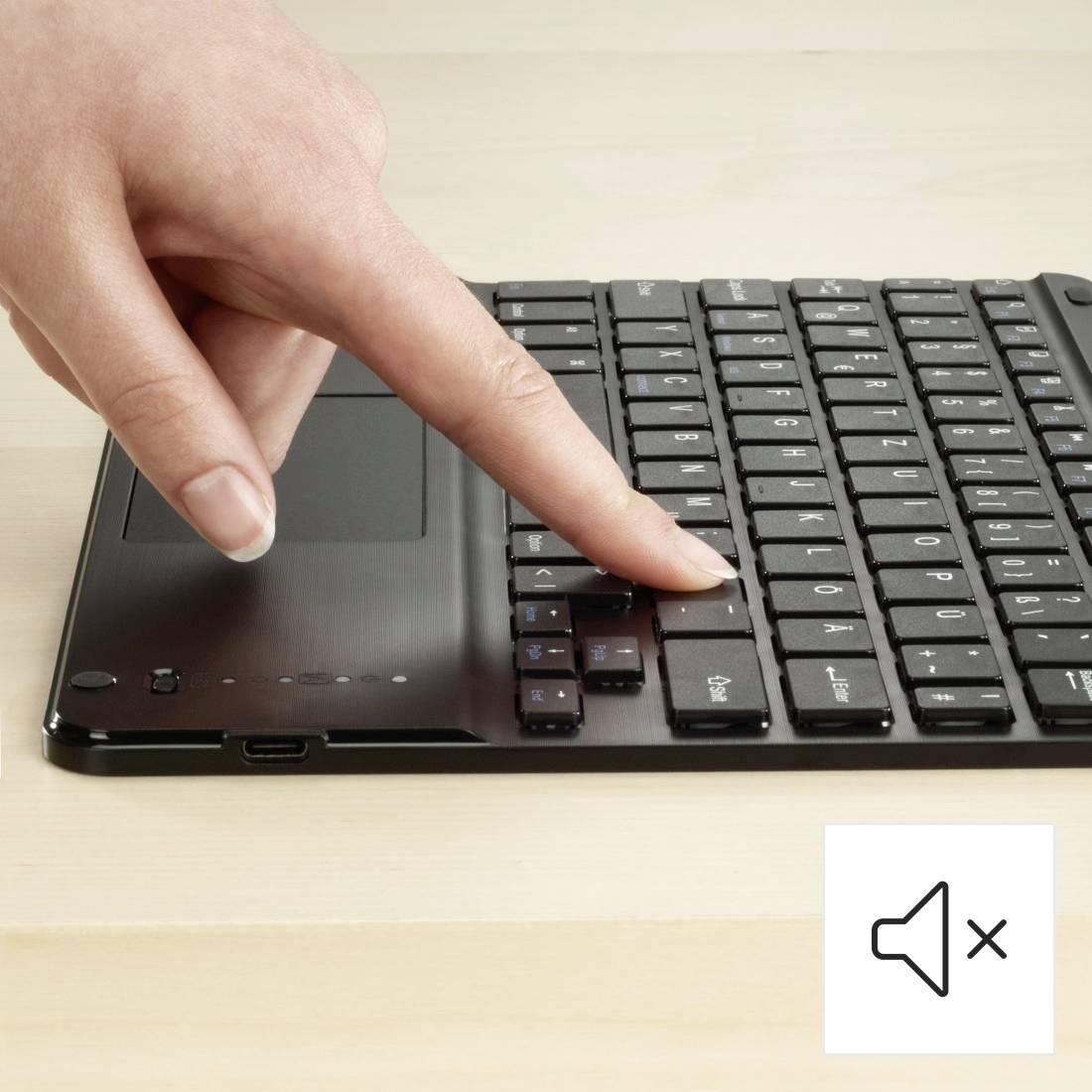 Eine Hand drückt die Stummschalttaste auf einer Laptop-Tastatur. Rechts unten ist ein Lautsprechersymbol mit einem Kreuz, das Stummschaltung anzeigt.