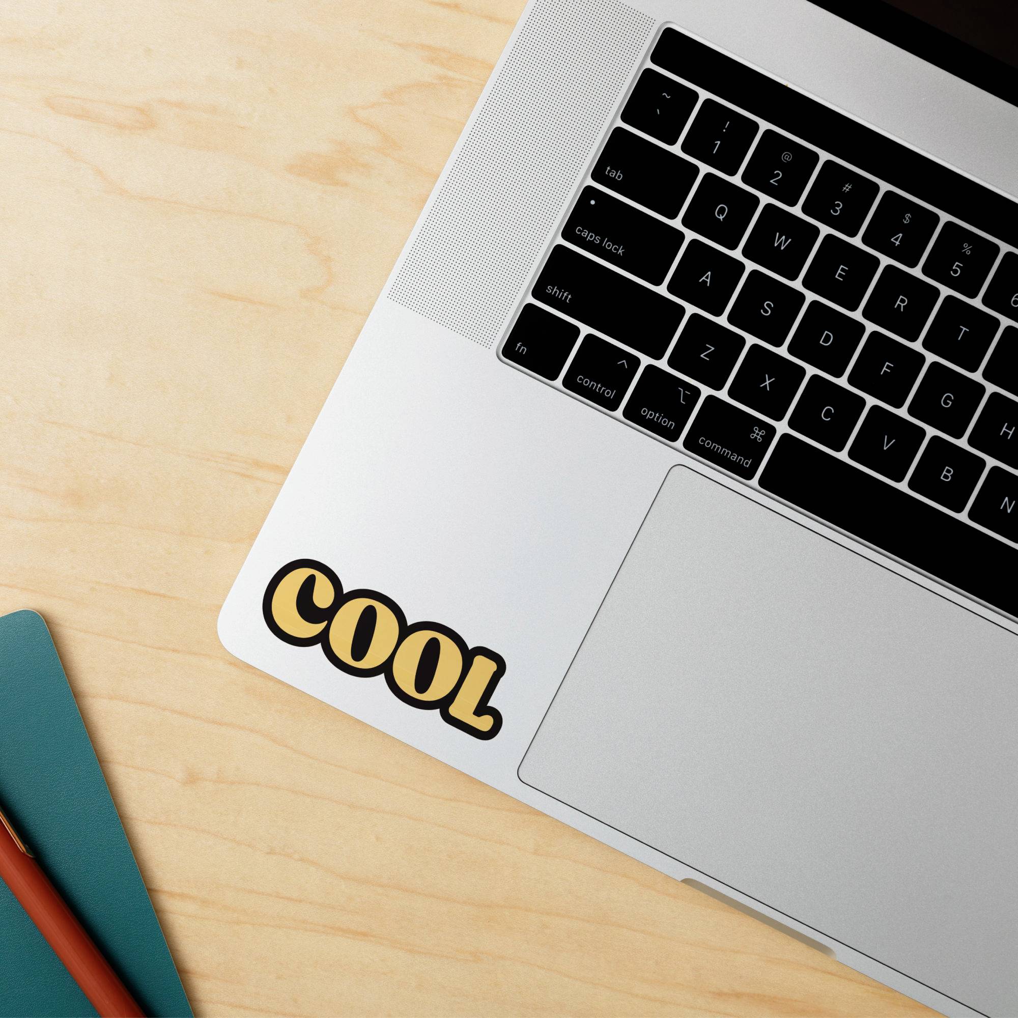 Laptop auf Holztisch mit Aufkleber 'COOL' auf der Ecke. Enges Bild auf Tastatur und Aufkleber fokussiert.