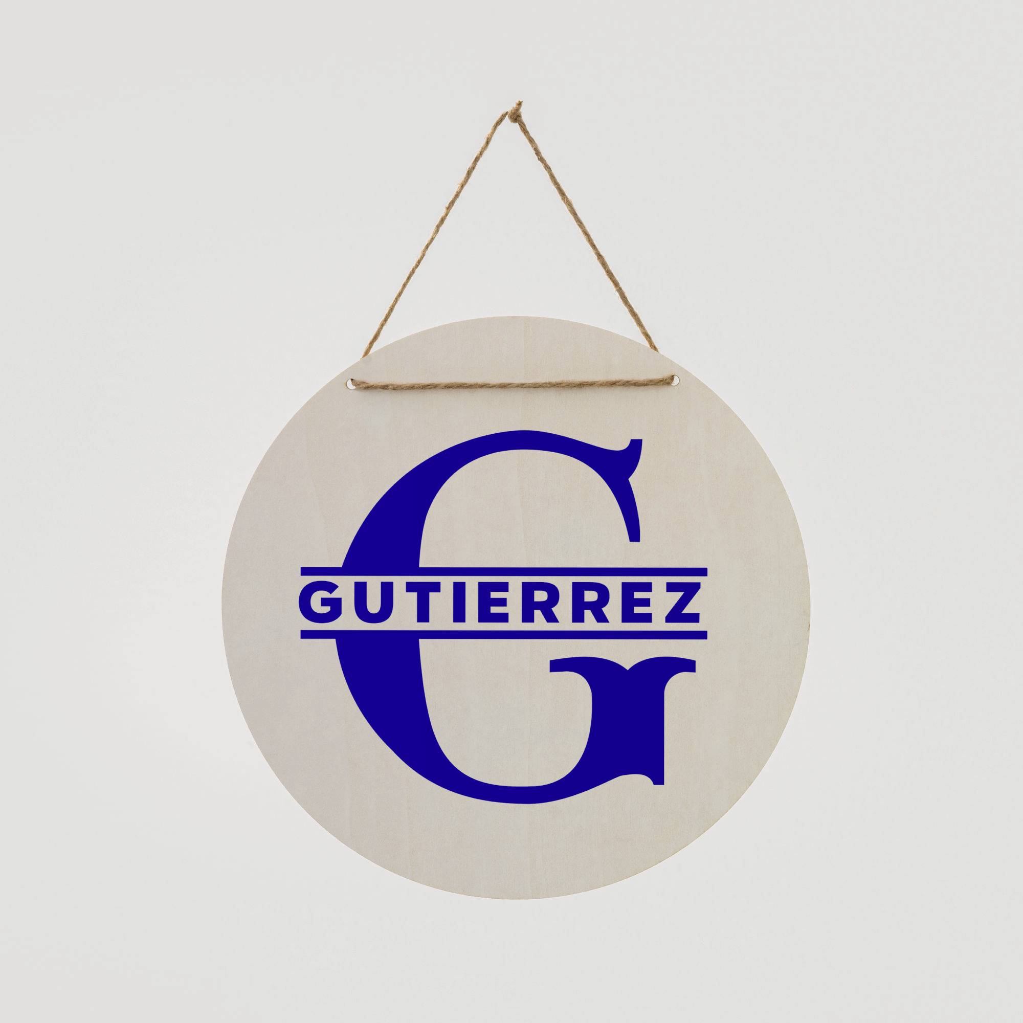 Ein rundes Holzschild hängt an einer Kordel. Darauf steht in blauer Schrift der Name 'Gutierrez' unter dem großen Buchstaben 'G'.