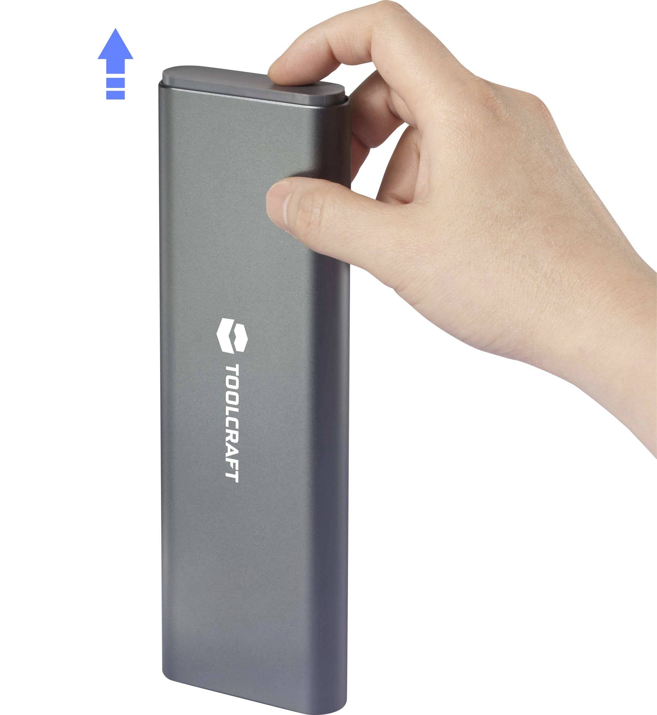 Hand hält ein rechteckiges, metallisches Werkzeug von Toolcraft, mit einer nach oben zeigenden Pfeilgrafik links oben im Bild.