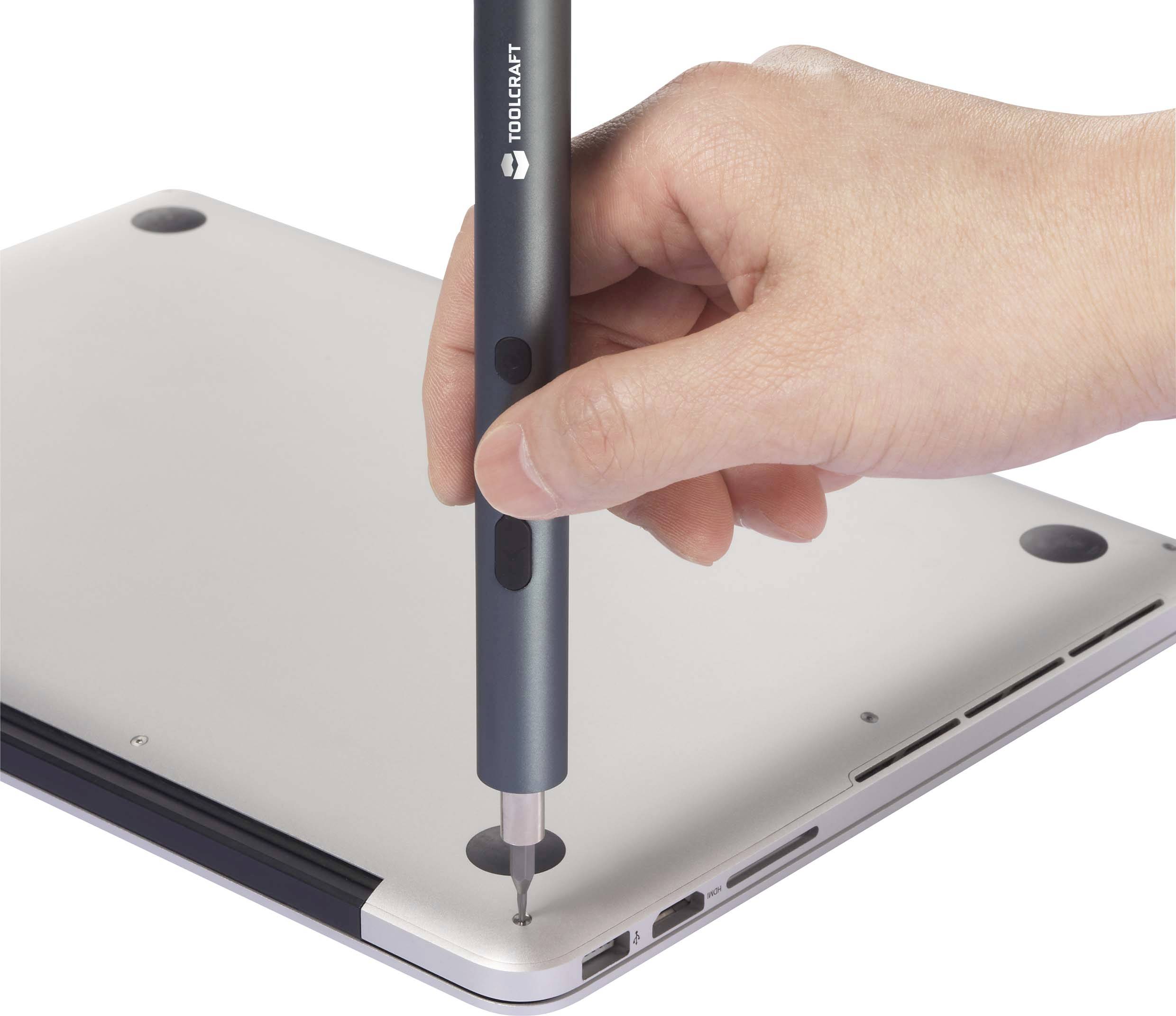 Eine Hand hält einen Schraubendreher, der verwendet wird, um eine Schraube an der Unterseite eines Laptops zu entfernen.