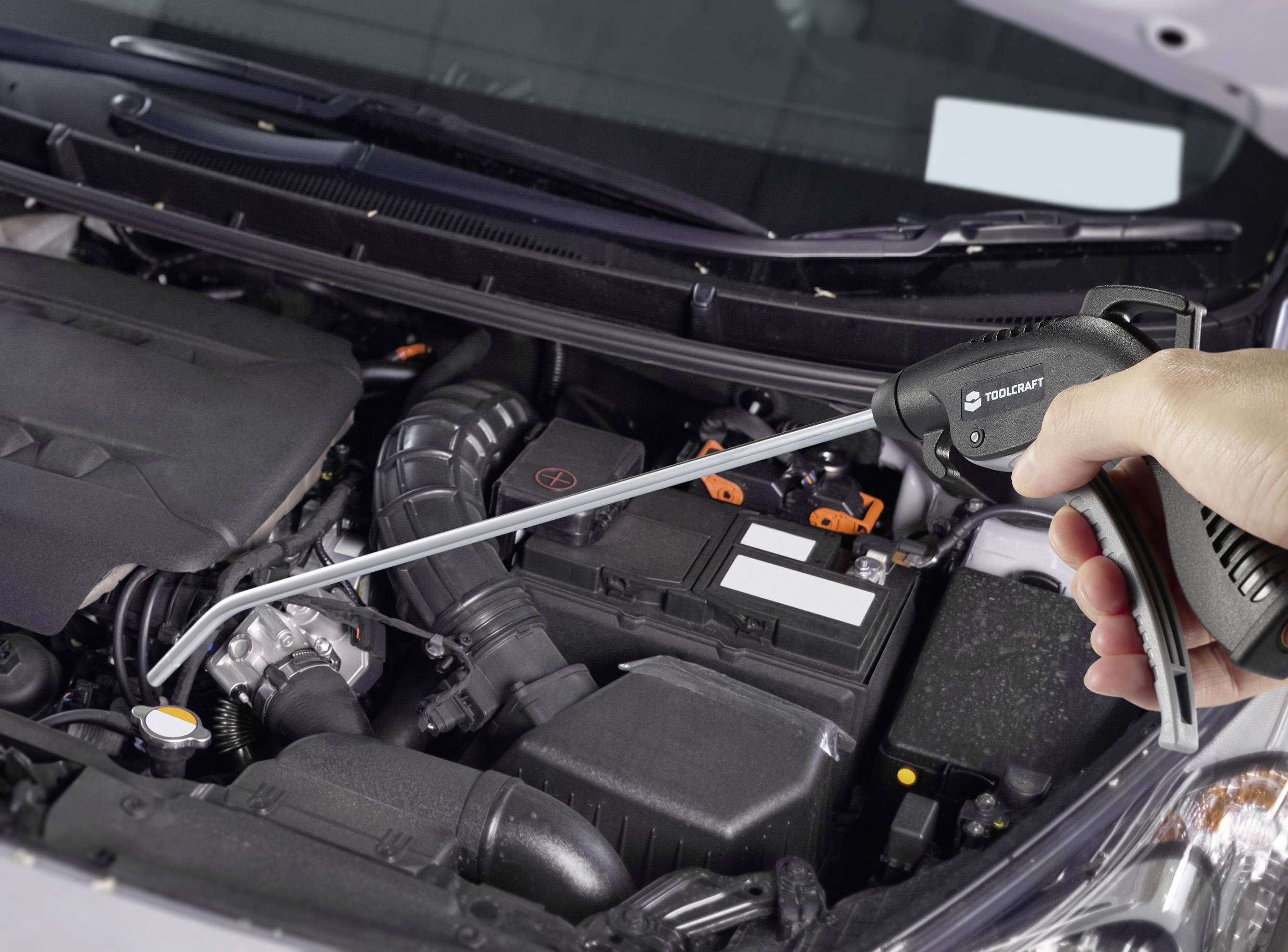 Hand hält eine Druckluftpistole über einem offenen Autokühler, bereit zur Reinigung im Motorraum.
