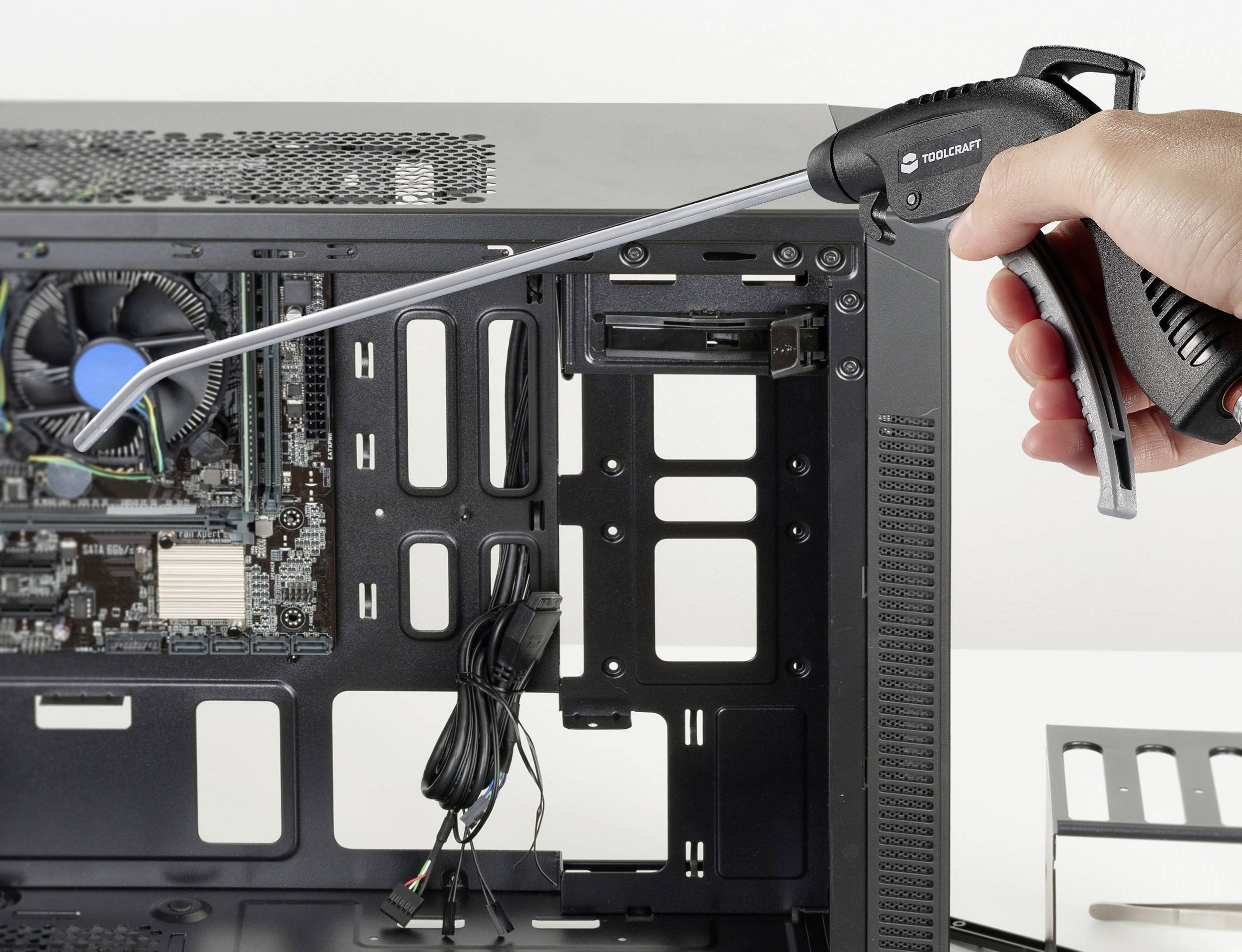 Eine Hand hält ein Druckluftspray und reinigt das Innere eines offenen Computergehäuses, um Staub von den Komponenten zu entfernen.