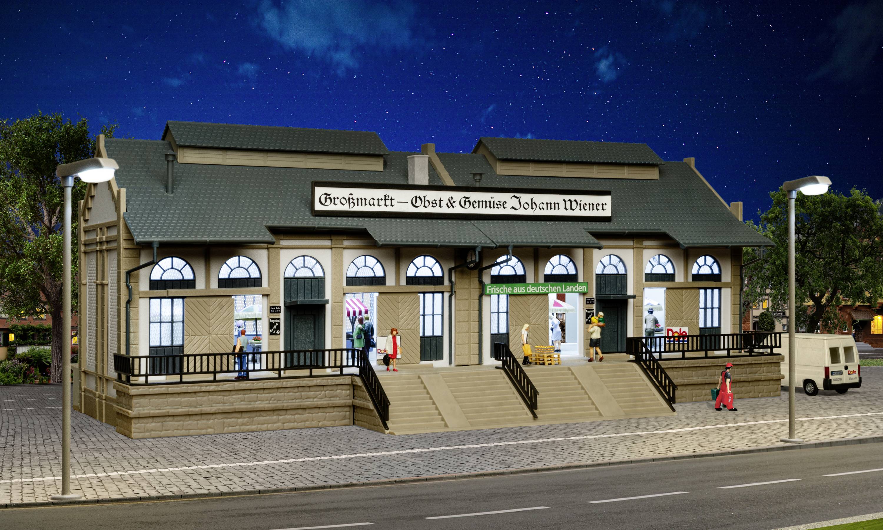 Ein beleuchtetes Gebäude bei Nacht mit der Aufschrift 'Großmarkt – Obst & Gemüse Johann Wienn'. Menschen und Lieferwagen davor.