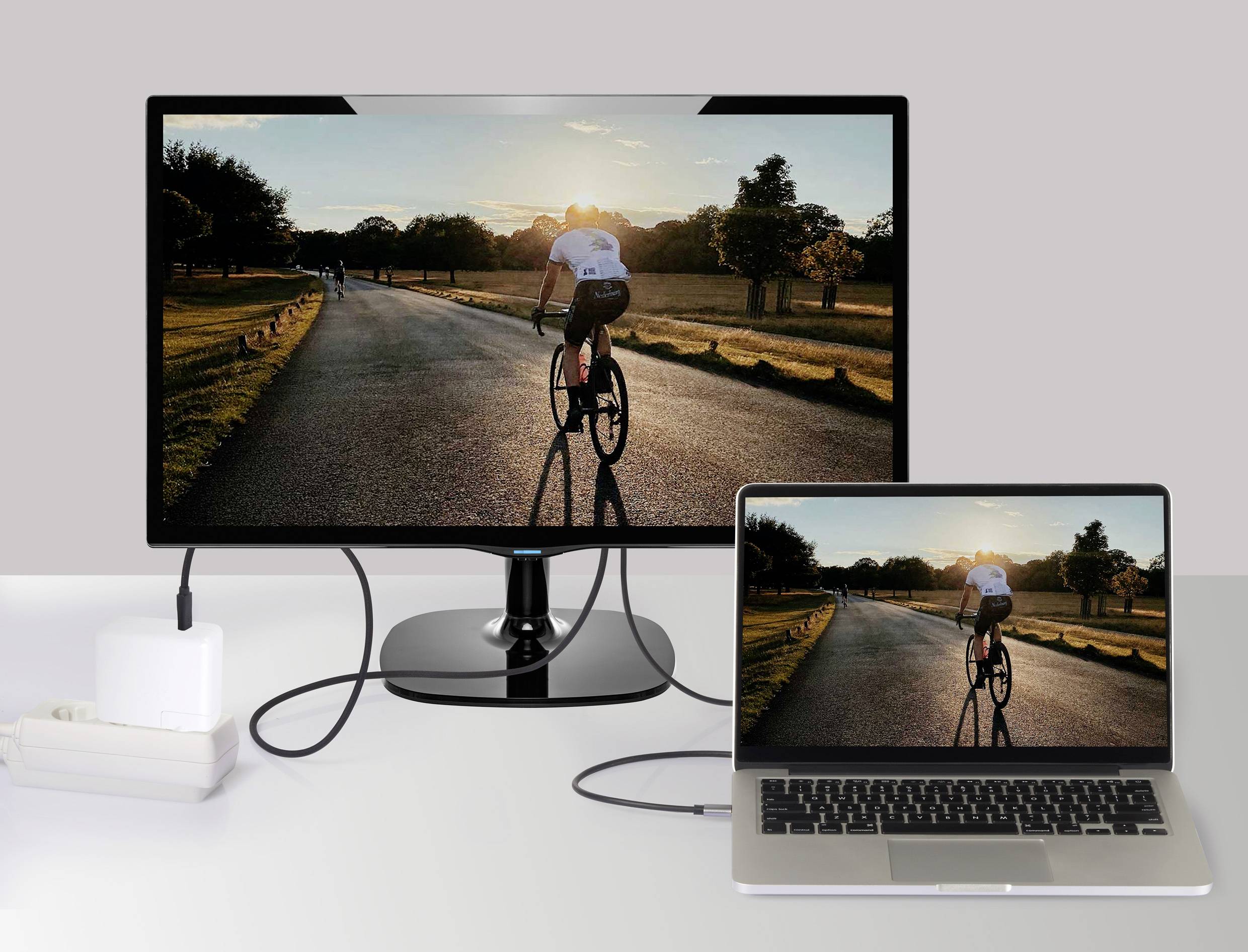 Ein Laptop und ein externer Monitor zeigen dasselbe Bild: eine Person, die bei Sonnenuntergang auf einer Straße Fahrrad fährt.