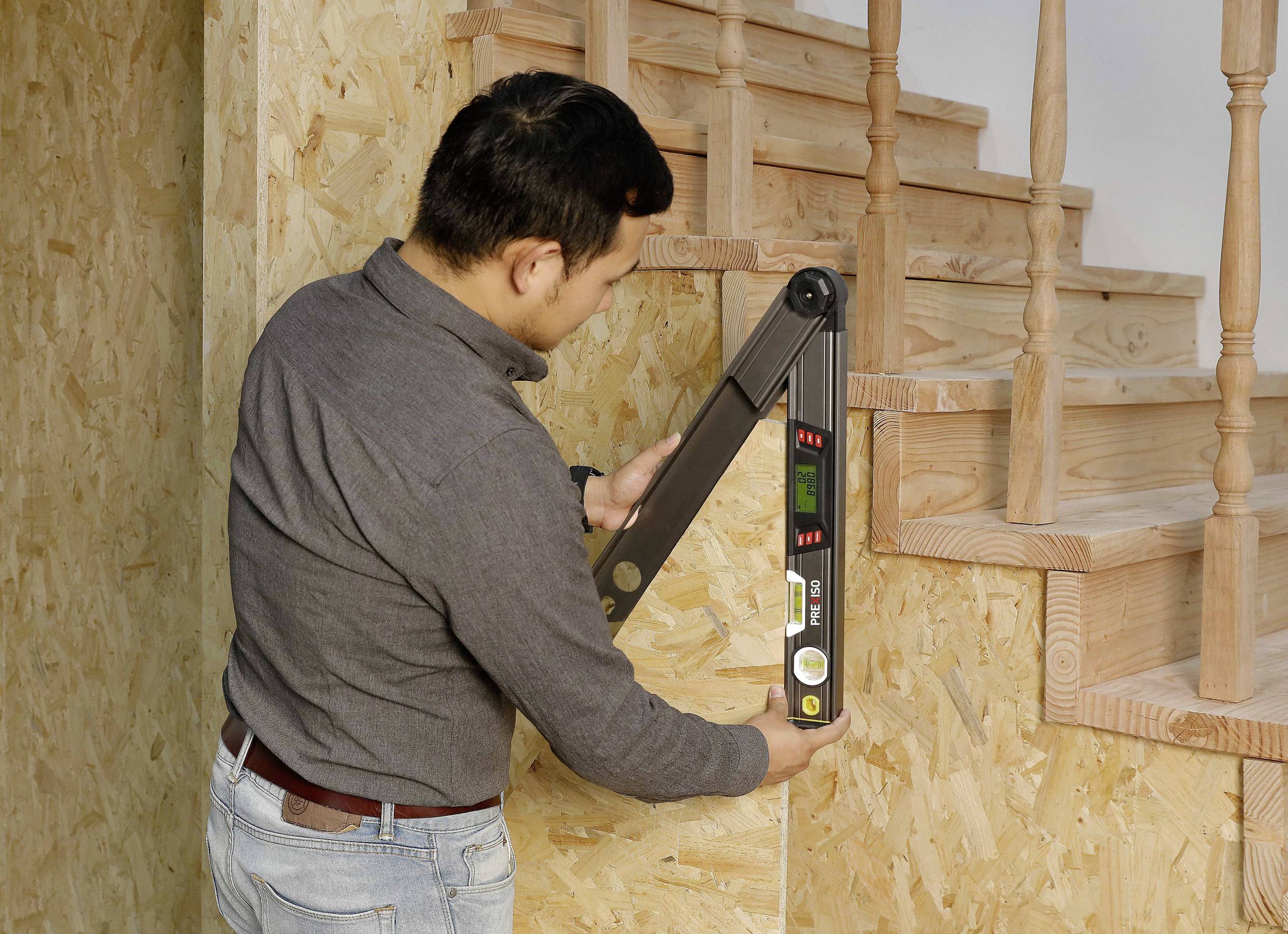 Ein Mann verwendet ein digitales Messwerkzeug, um den Winkel einer Treppe aus Holz zu messen.