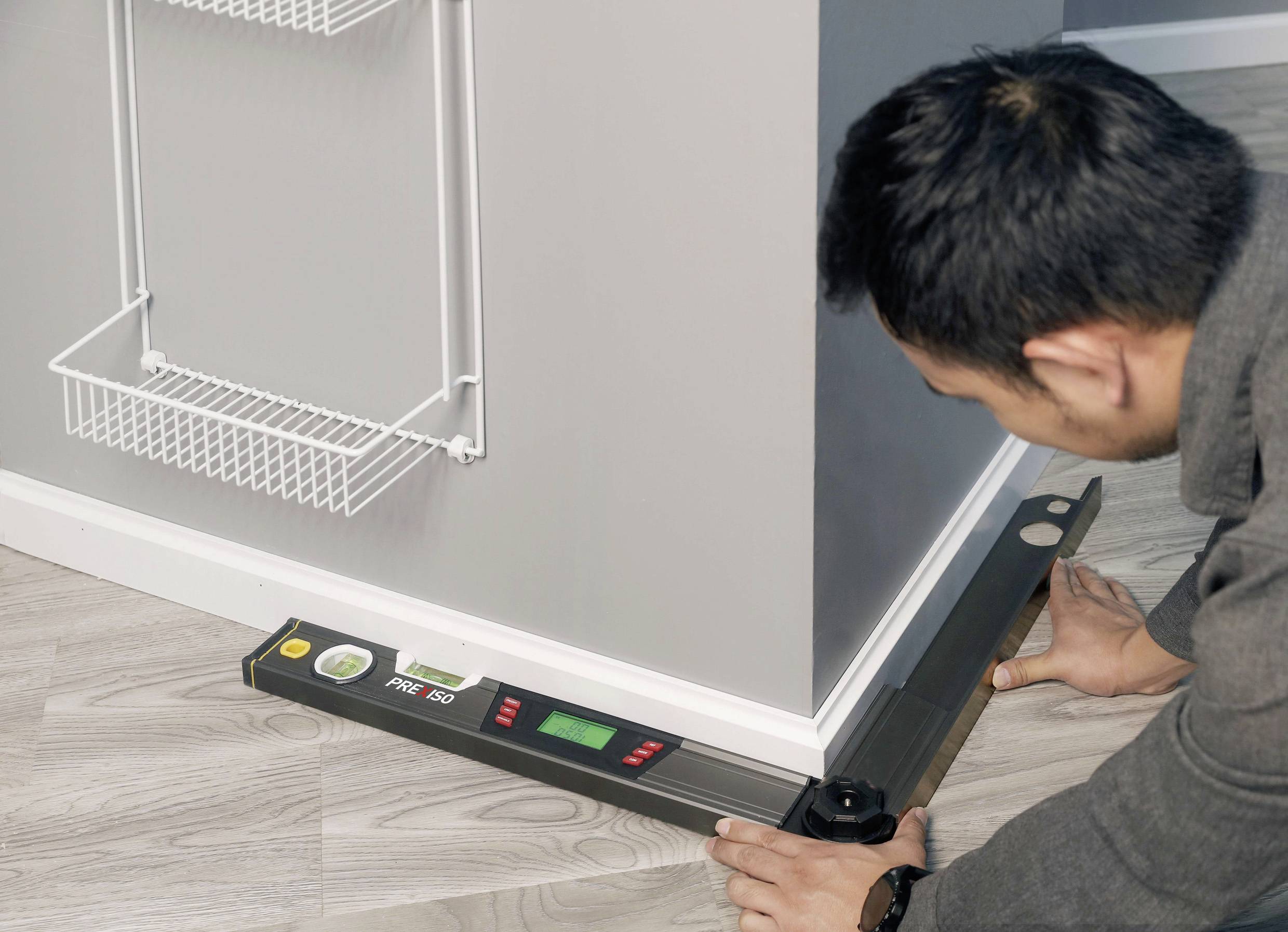 Eine Person misst den Winkel eines Raumesckens mit einem digitalen Winkelmesser auf einem Holzboden.