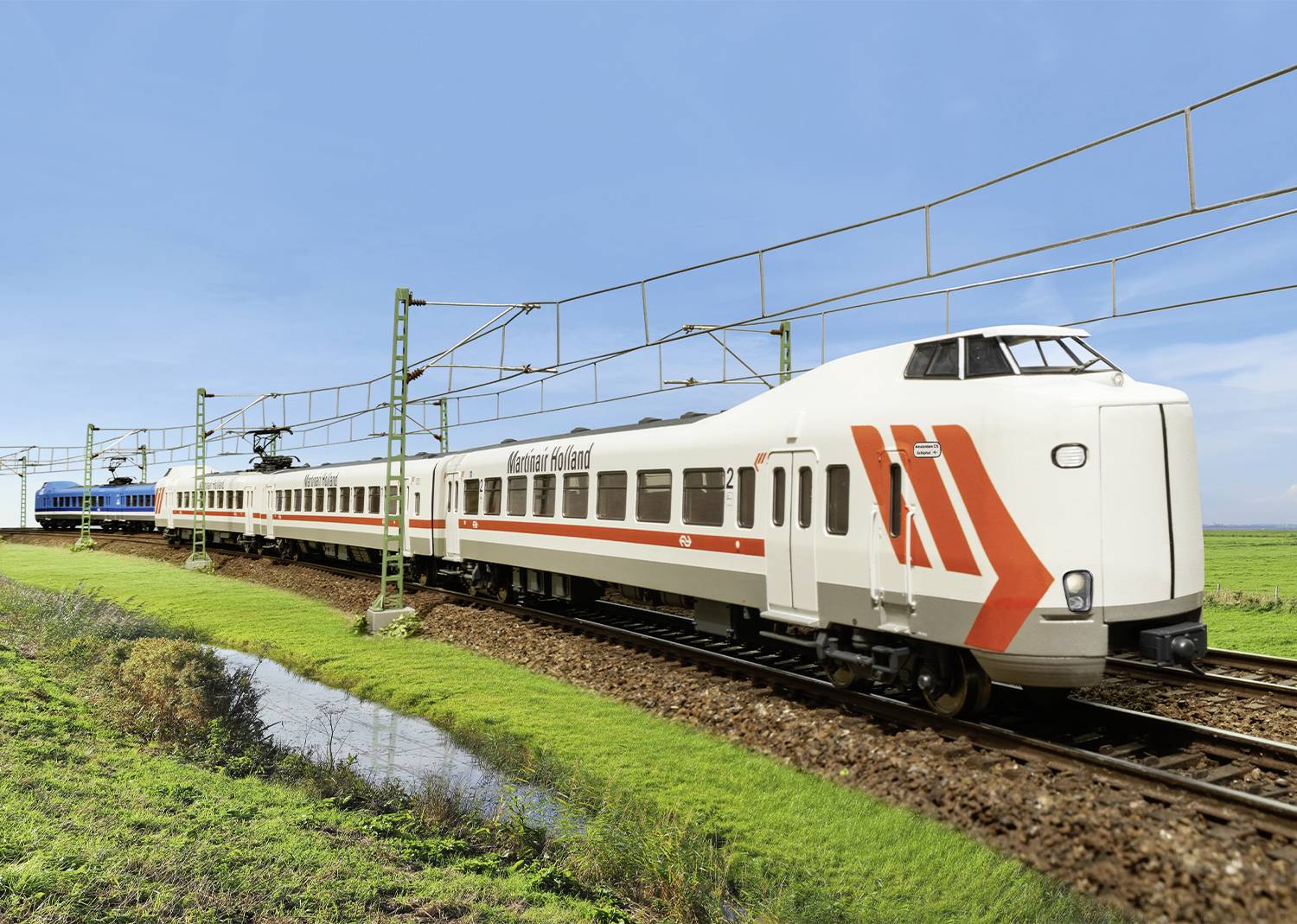 Ein weißer Zug mit roten Streifen fährt auf einem Gleis durch eine grüne Landschaft, blauer Himmel im Hintergrund.