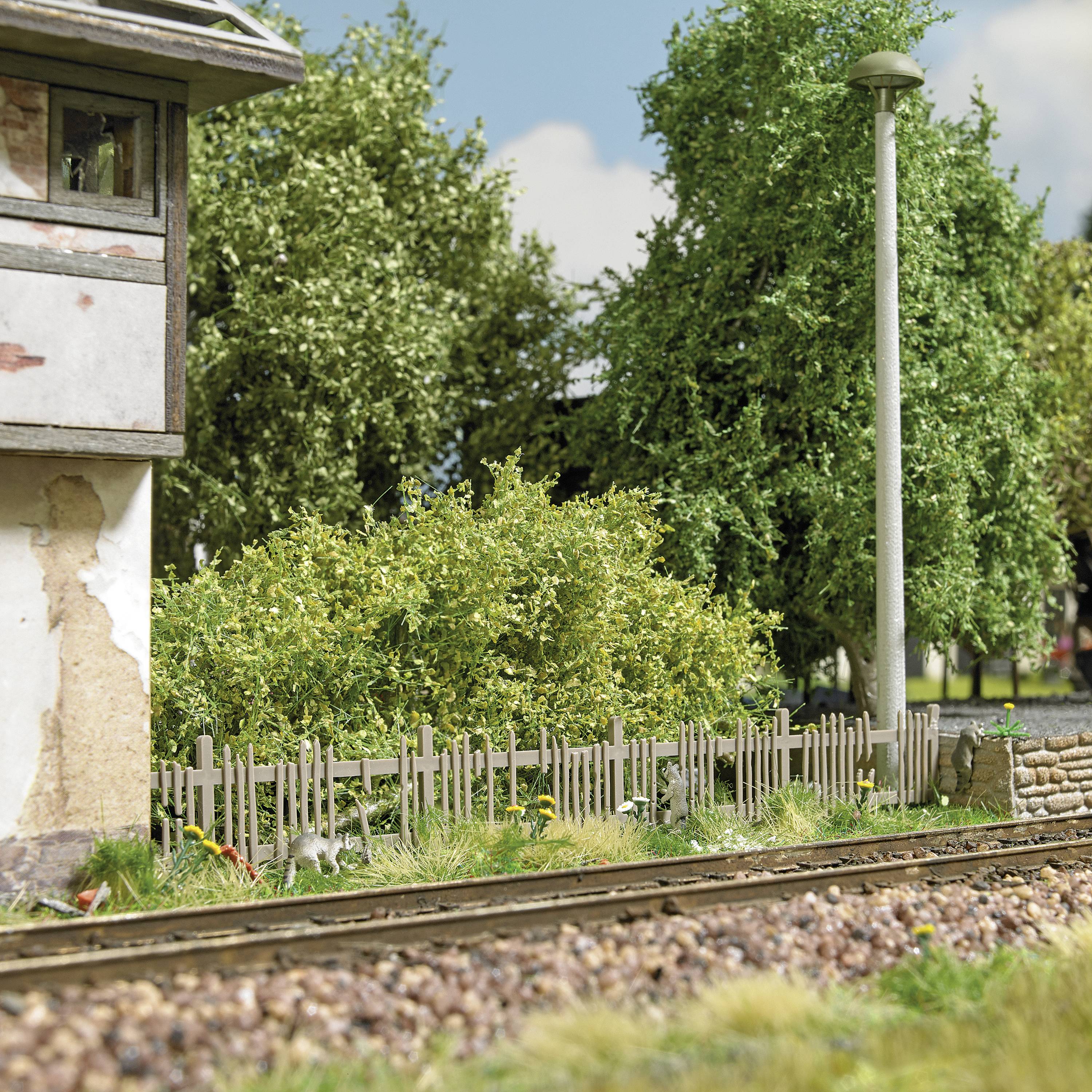 Ein stillgelegtes Bahngleis neben einer verwitterten Mauer und dichtem Gebüsch mit Bäumen im Hintergrund an einem sonnigen Tag.