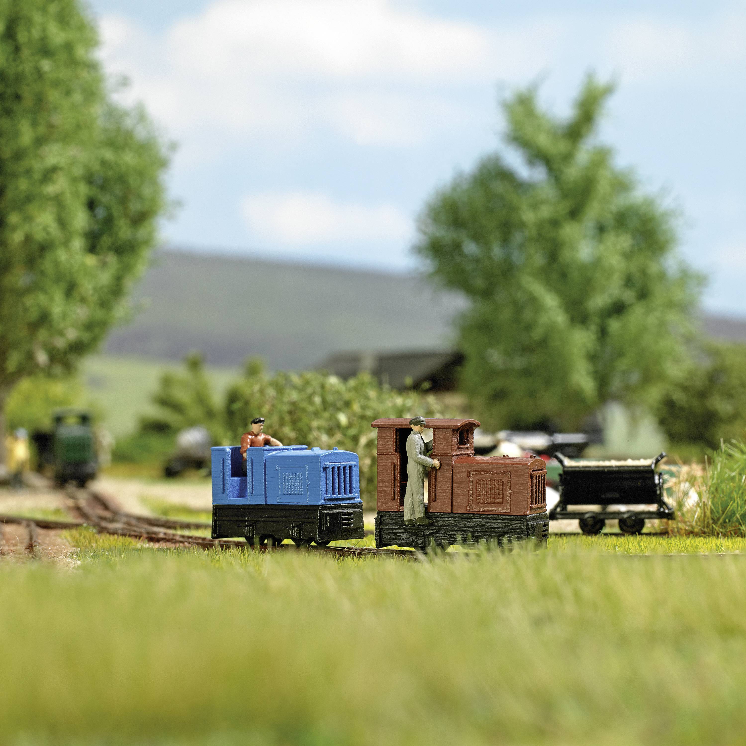 Eine Miniatureisenbahn mit zwei Lokomotiven auf einem Gleis in einer ländlichen Kulisse mit Bäumen und einem Hügel im Hintergrund.