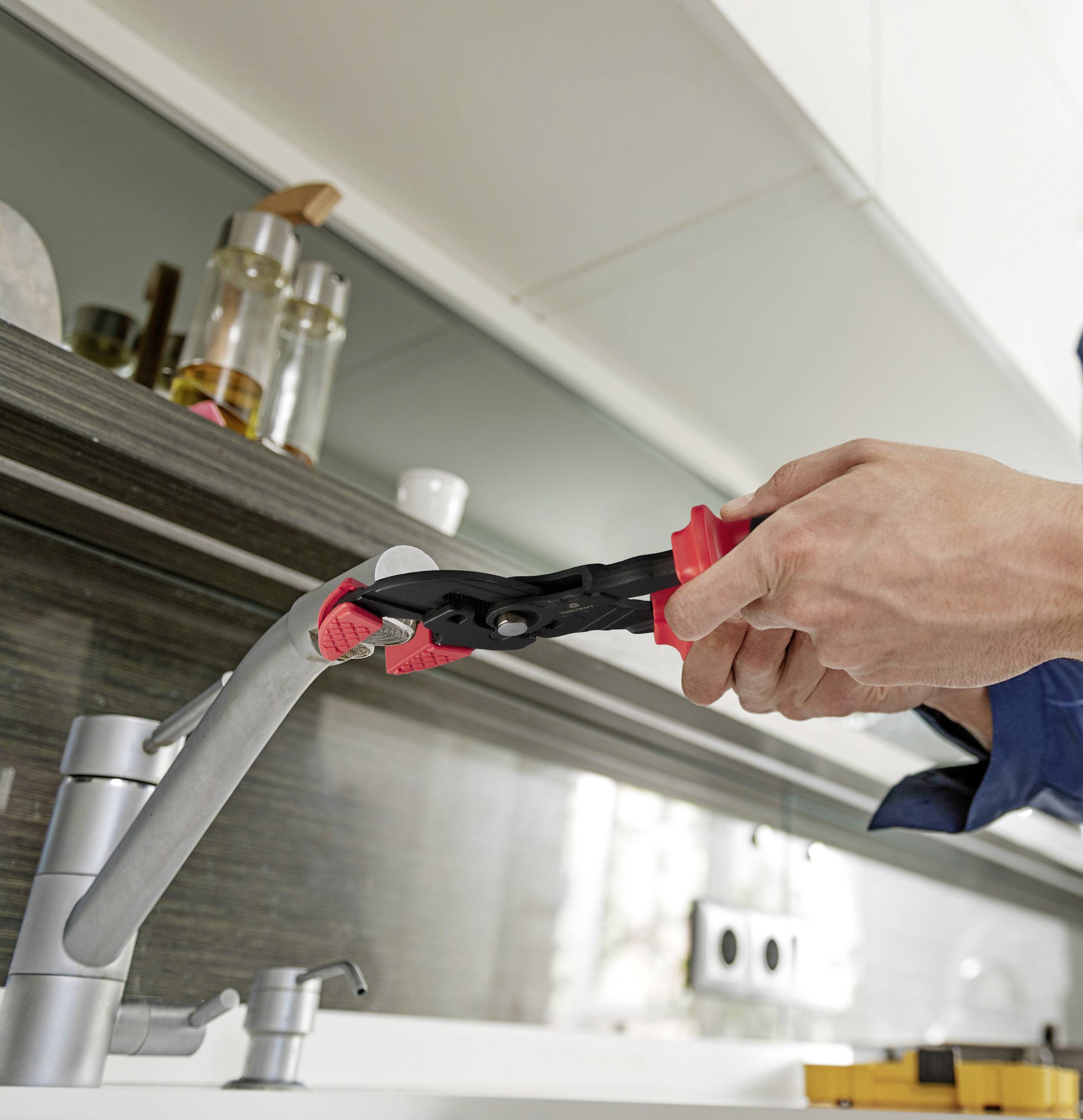 Eine Person benutzt eine Rohrzange, um einen Wasserhahn in einer Küche zu reparieren.