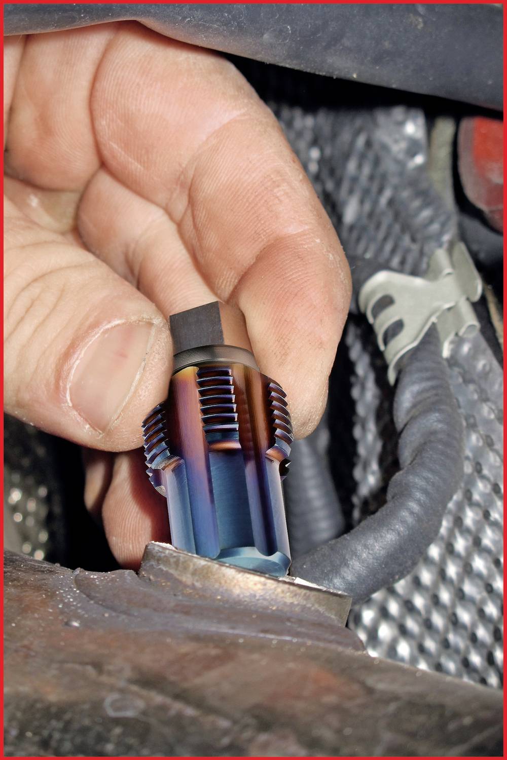 Nahaufnahme einer Hand, die einen metallischen Autoteilzylinder hält, der in der Nähe eines Kabels installiert wird.