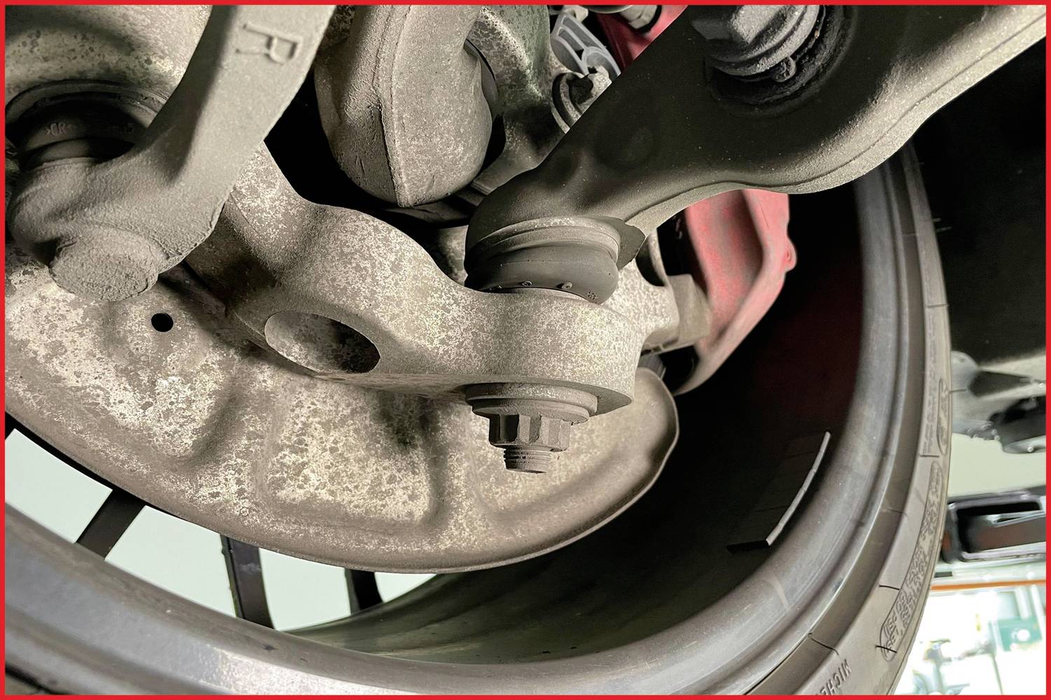 Nahaufnahme eines Autoreifens und der Aufhängung im Profil, mit sichtbaren Teilen der Bremse. Fokussiert auf technische Details.
