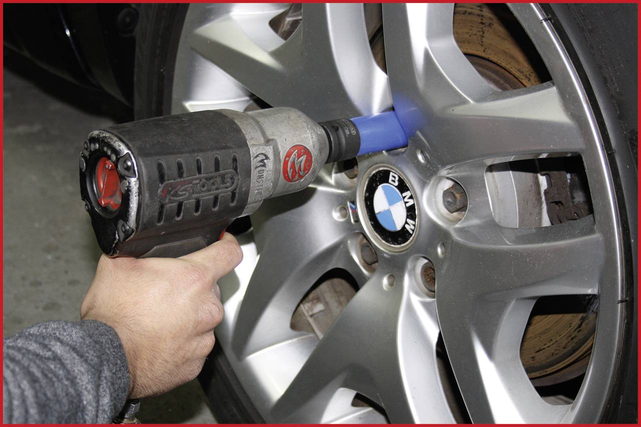 Eine Nahaufnahme zeigt einen Akkubohrer, der eine Radschraube an einem BMW-Autoreifen anzieht.