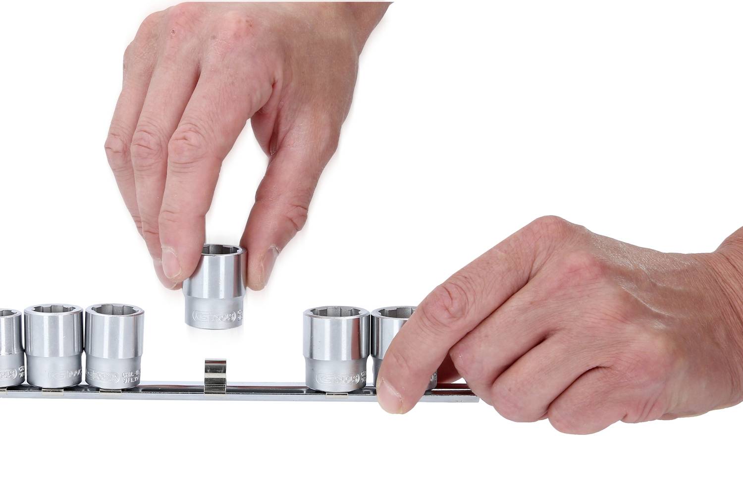 Zwei Hände ordnen Steckschlüssel auf einer Halterung an. Eine Hand hebt einen Steckschlüssel an, die andere hält die Halterung.