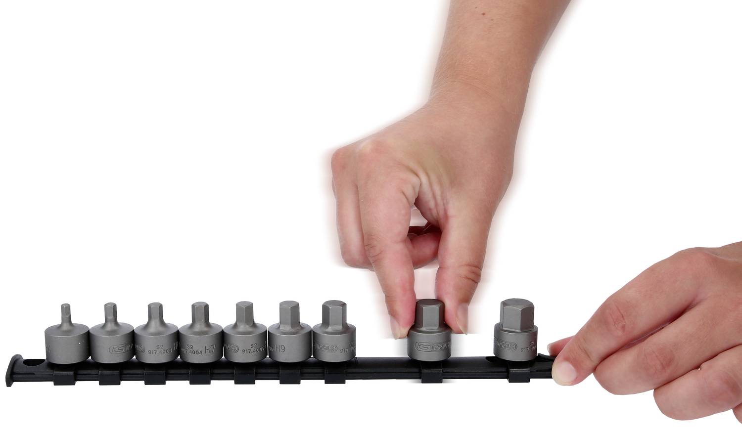 Eine Hand setzt einen Steckschlüssel auf eine Halterung mit mehreren Steckschlüsseln unterschiedlicher Größe.