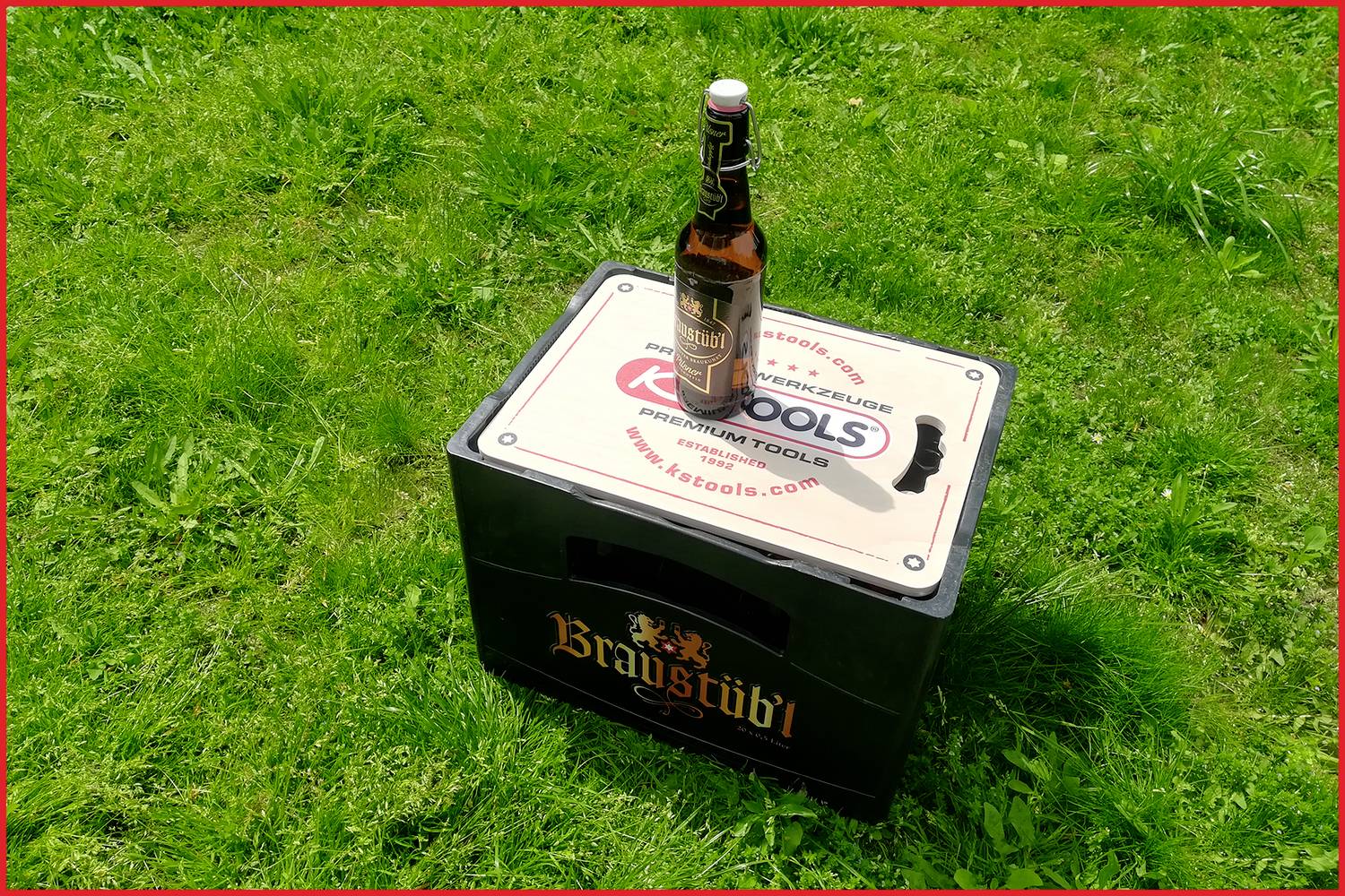 Eine geschlossene Bierkiste der Marke 'Braystädtl' steht auf einer Wiese. Eine einzelne Bierflasche steht oben auf der Kiste.