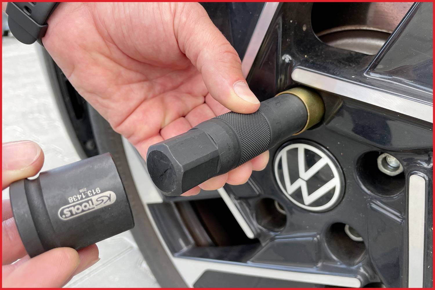 Zwei Hände wechseln einen Autoreifen: Eine Hand hält einen Radschraubenschlüssel, die andere einen Adapter an einer schwarzen Felge.