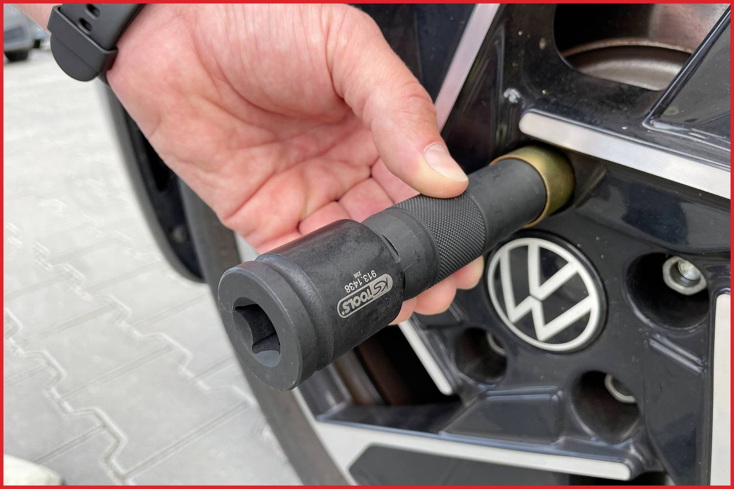 Eine Hand hält einen Drehmomentschlüssel und zieht eine Radmutter an einer Autofelge mit einem VW-Logo fest.