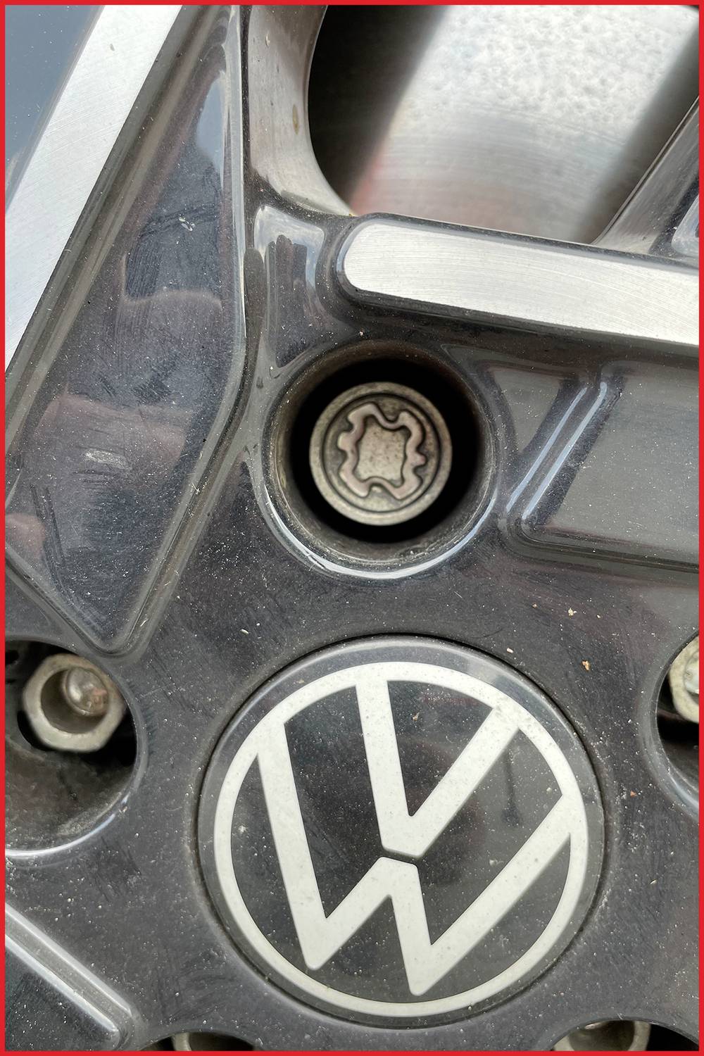 Nahaufnahme eines VW-Logos auf einer Auto-Radkappe mit einem zentralen Nabenabdeckungs-Schraubenschlüssel im oberen Teil sichtbar.