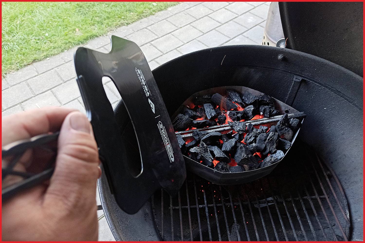 Grill mit glühenden Kohlen; jemand benutzt Anzündkamin, um Kohlen zu erhitzen.