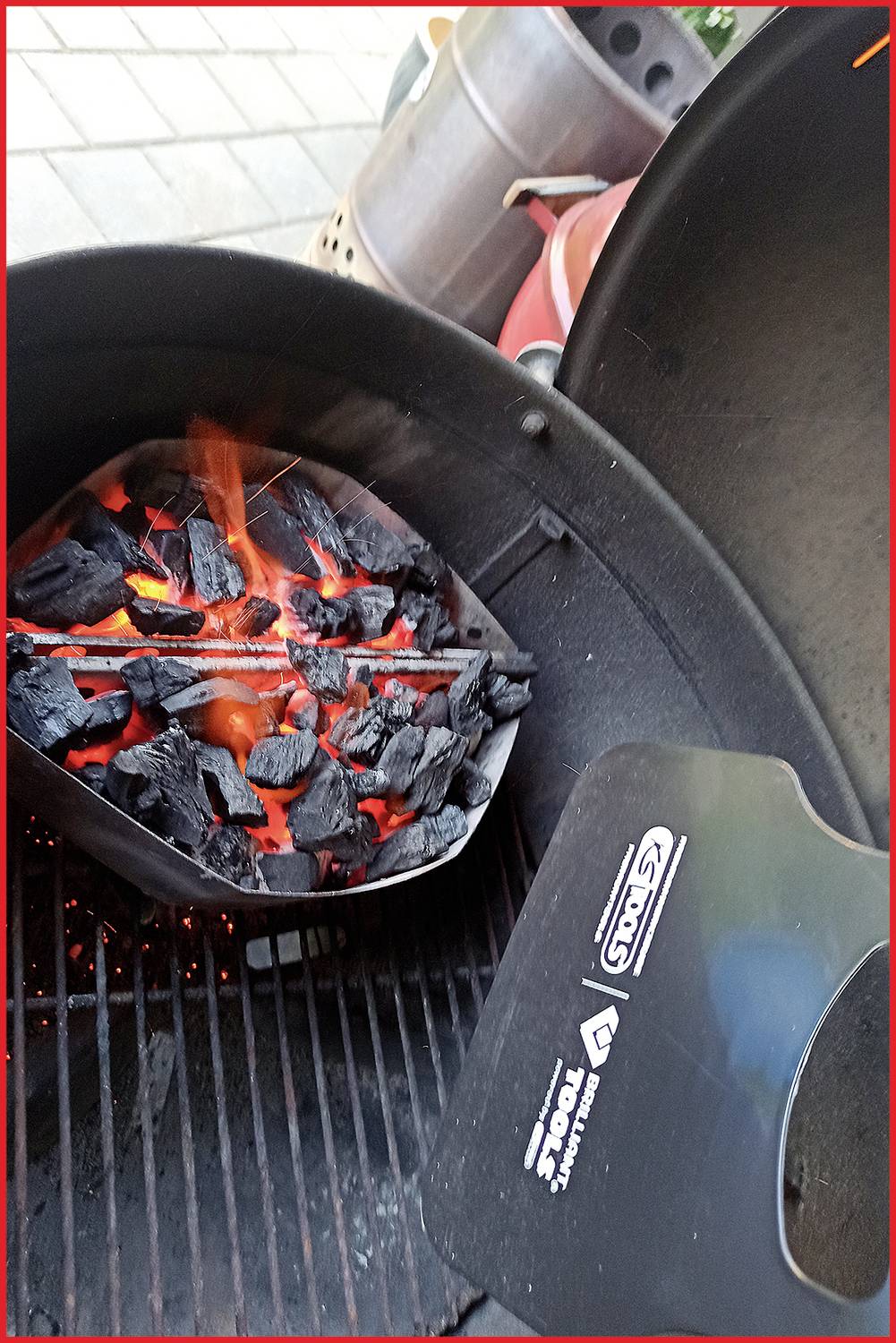 Ein Grill mit glühender Kohle, seitlich ein Grillrost und Grillzange in Sicht. Es sind Flammen und leuchtende Kohlen zu sehen.