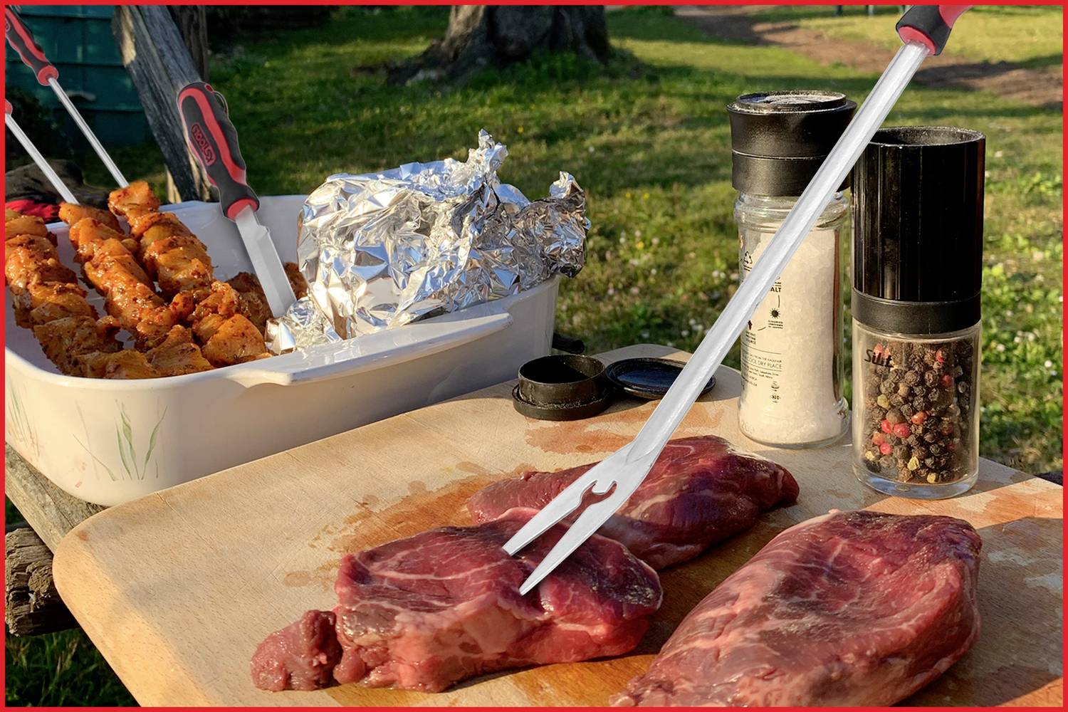 Ein Holztisch im Freien mit rohem Fleisch, einer Fleischgabel, Gewürzen und vorbereiteten Grillspießen auf einem Grilltablett.