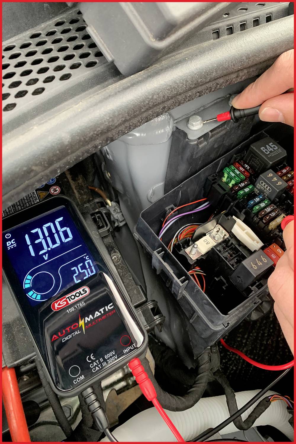 Eine Person misst die Spannung einer Autobatterie mit einem digitalen Multimeter. Das Display zeigt 13,06 V an.