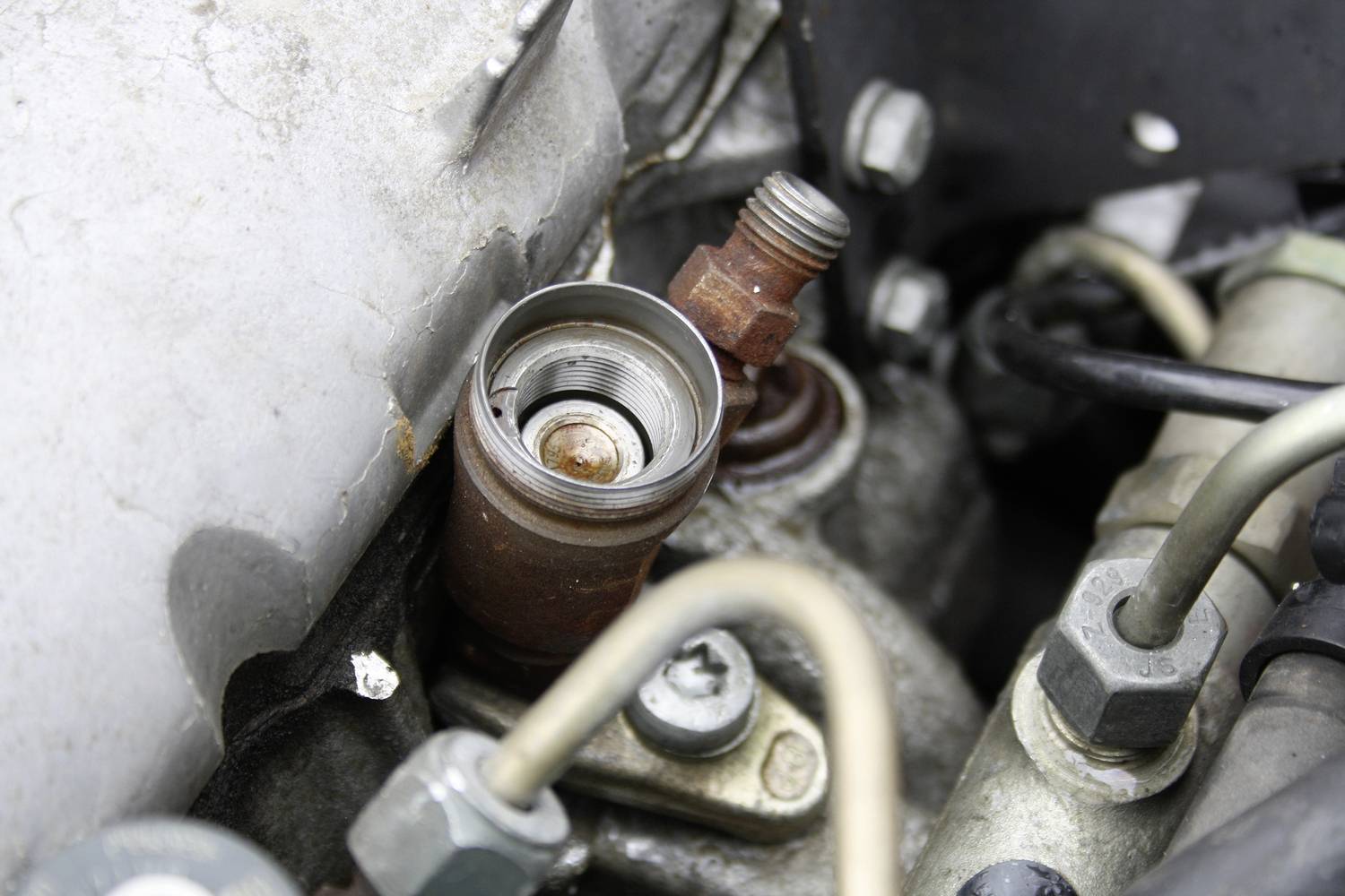 Nahaufnahme eines Motorenteils mit einer rostigen Schraube und mehreren Metallrohren. Das Bild zeigt Details eines technischen Mechanismus.