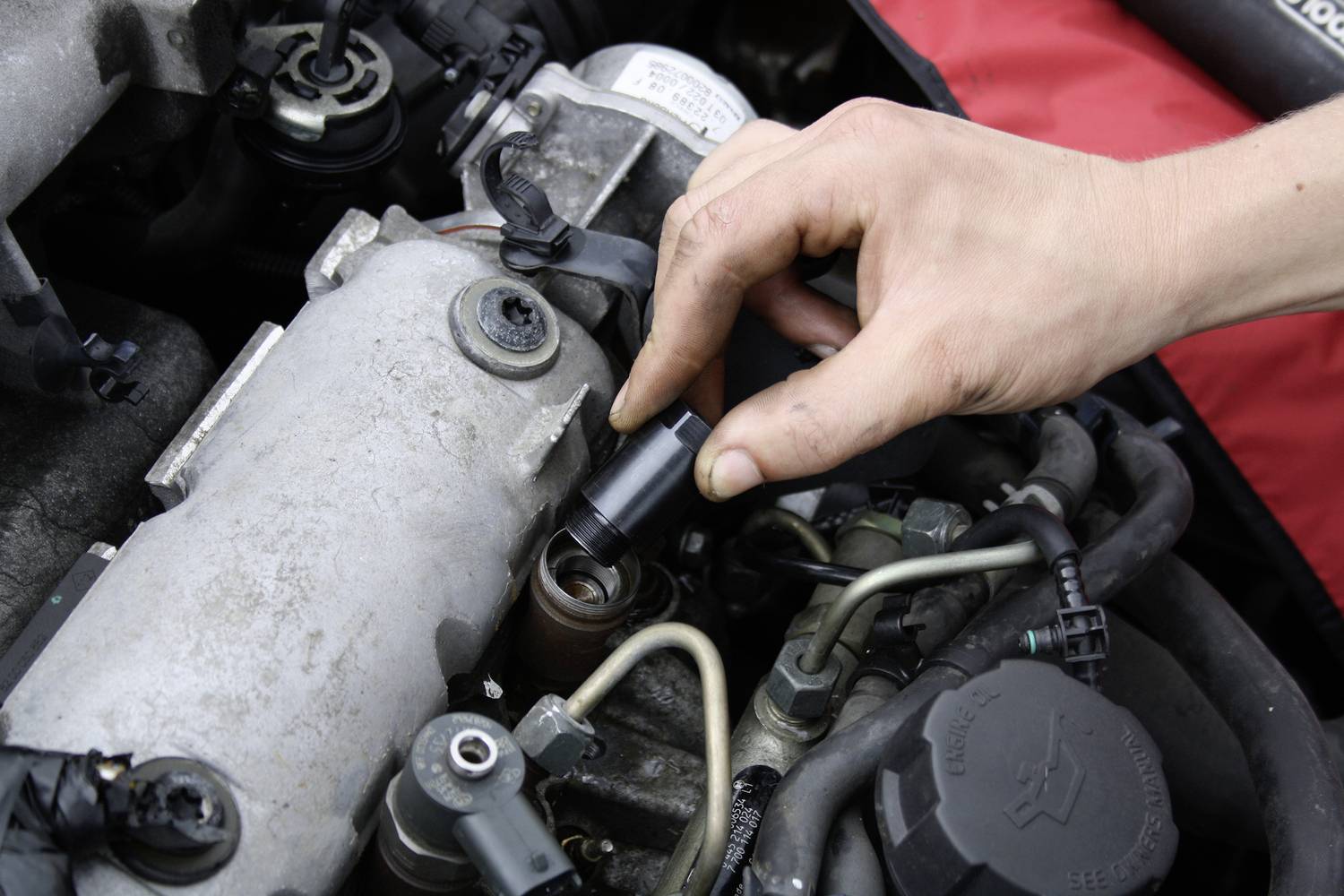 Eine Hand repariert oder inspiziert den Motor eines Autos, indem sie Teile des Motors unter dem geöffneten Deckel justiert.