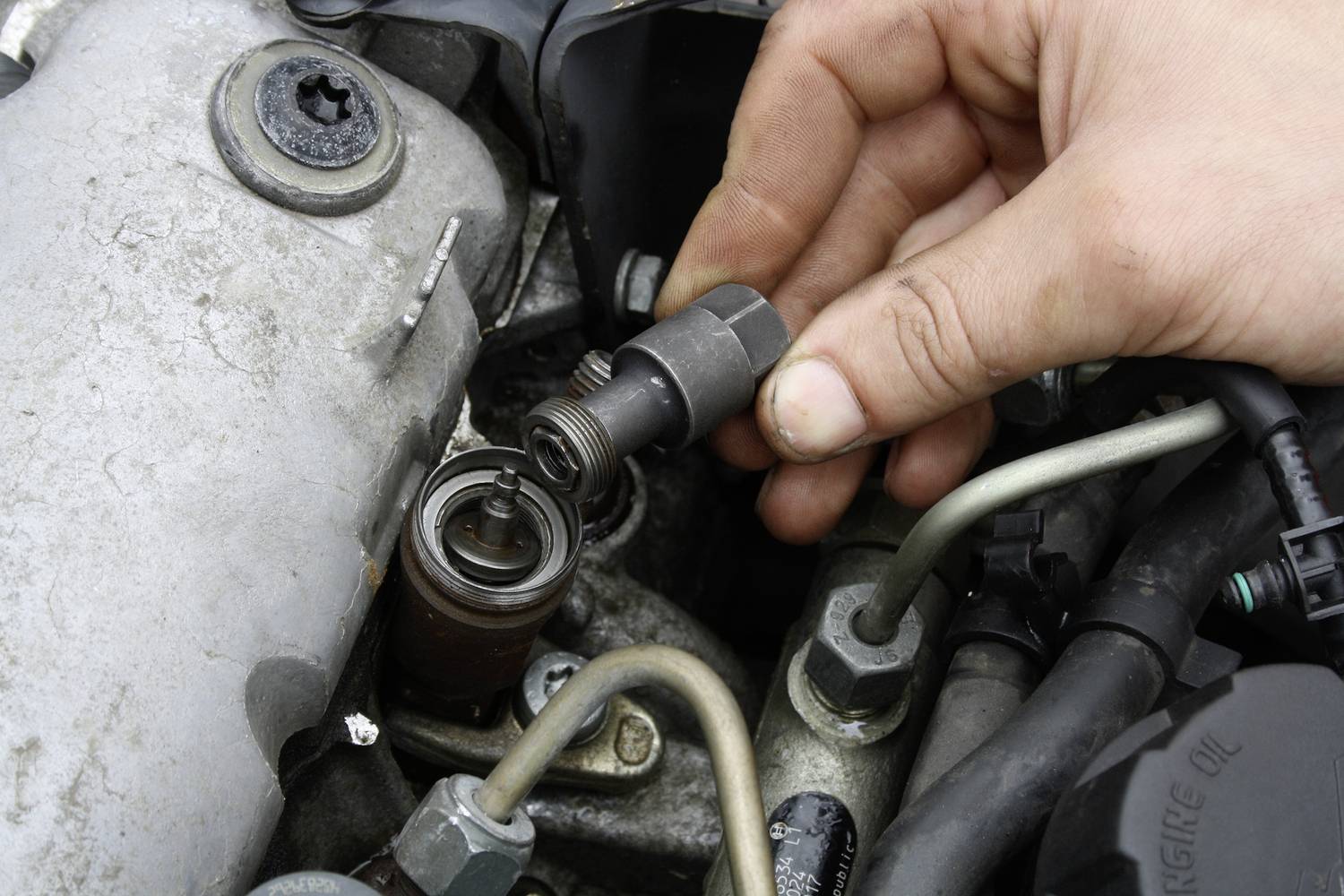 Eine Hand wechselt eine Zündkerze in einem Motorraum, umgeben von Metallteilen und Kabeln, im Rahmen einer Fahrzeugwartung.