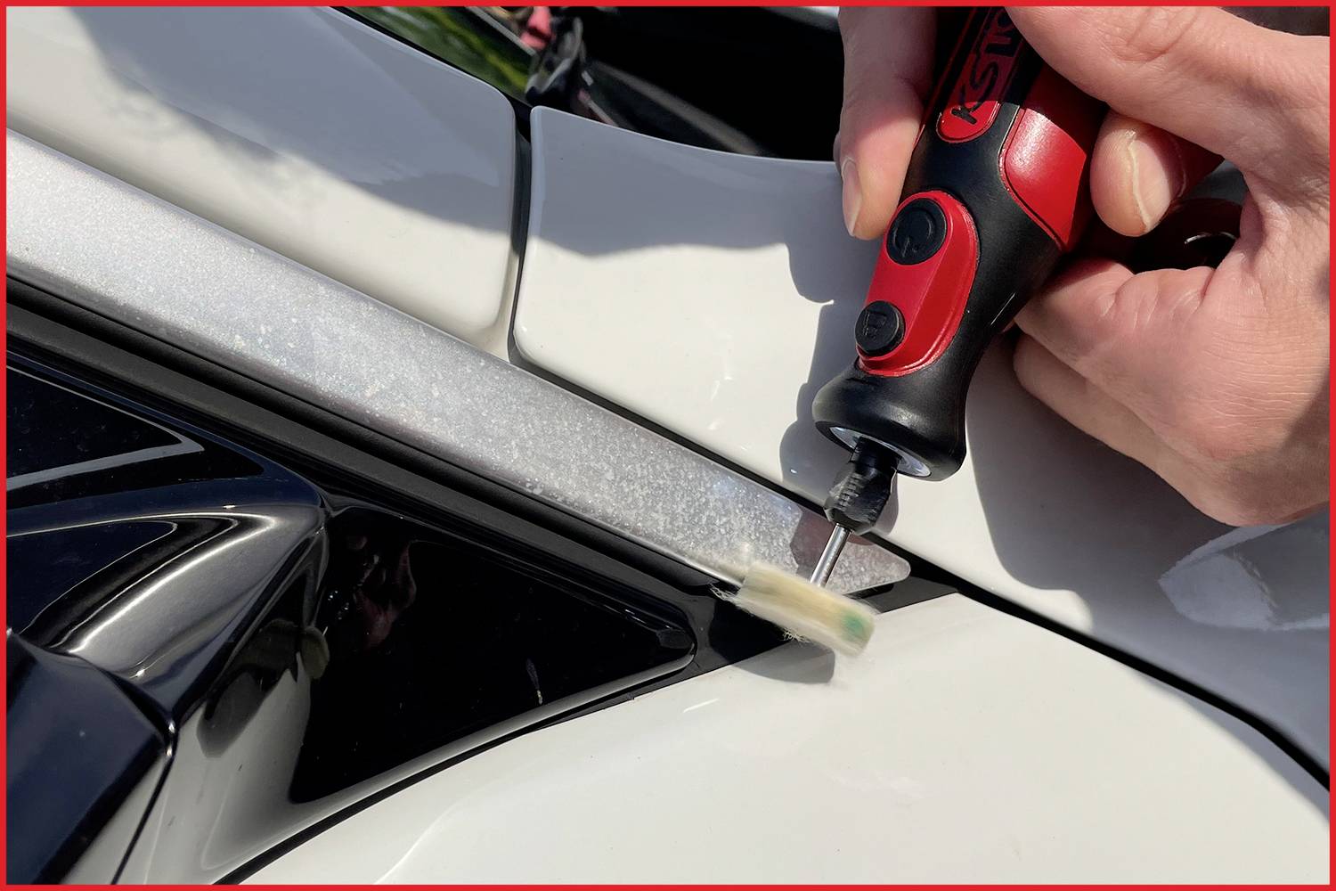 Nahaufnahme einer Person, die ein kleines Elektrowerkzeug benutzt, um ein Bauteil an einem weißen Auto anzupassen oder zu reparieren.