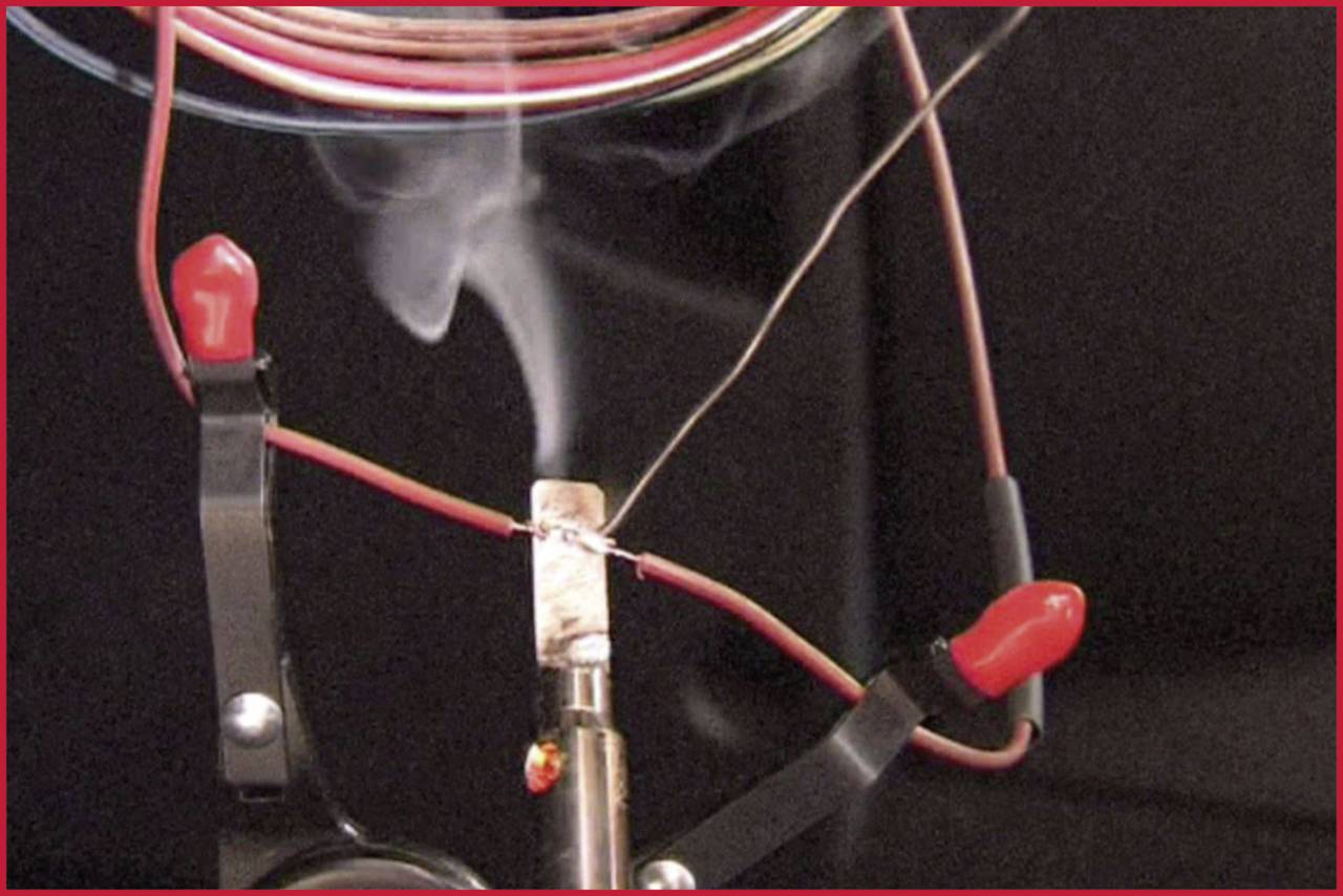 Rauch steigt von einem erhitzten Draht auf, der von Krokodilklemmen gehalten wird. Elektrisches Experiment zur Demonstration von Stromfluss.