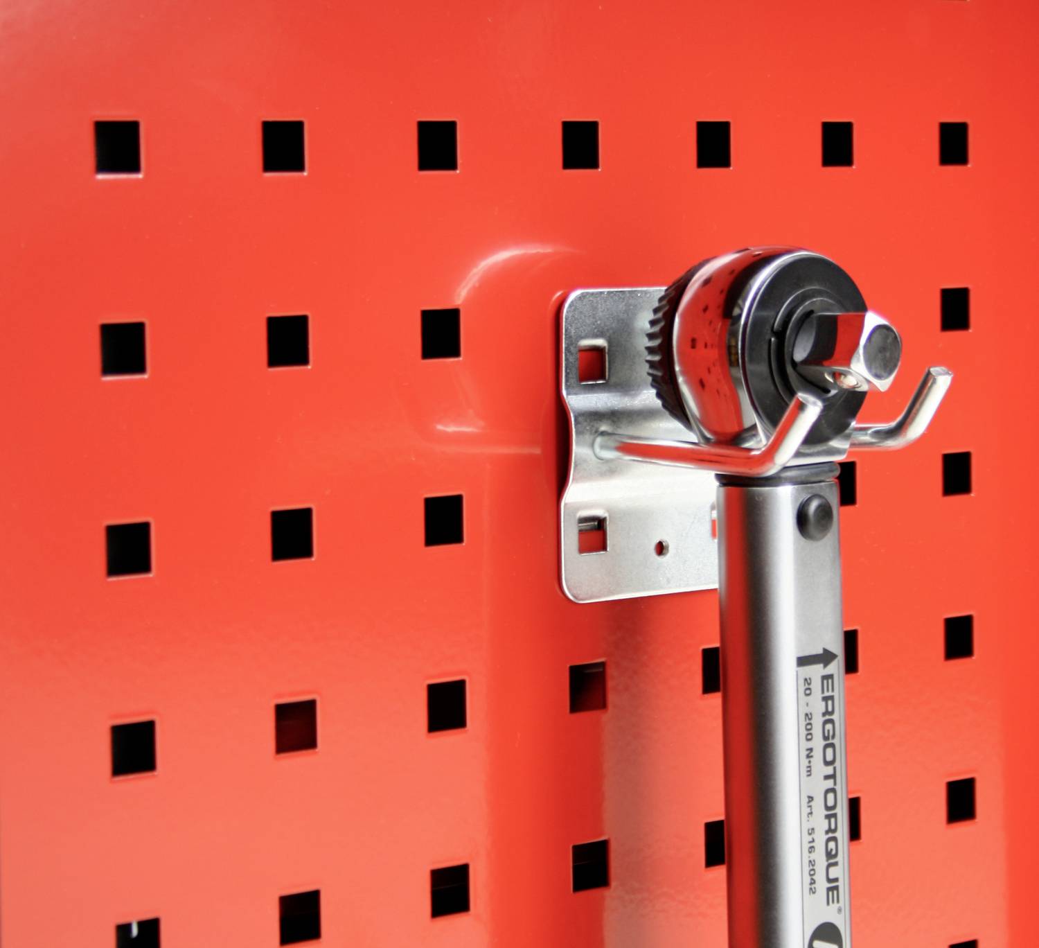 Drehmomentschlüssel hängt an einer roten Lochwand, befestigt mit einer Metallhalterung. Das Werkzeug ist bereit zur Entnahme.