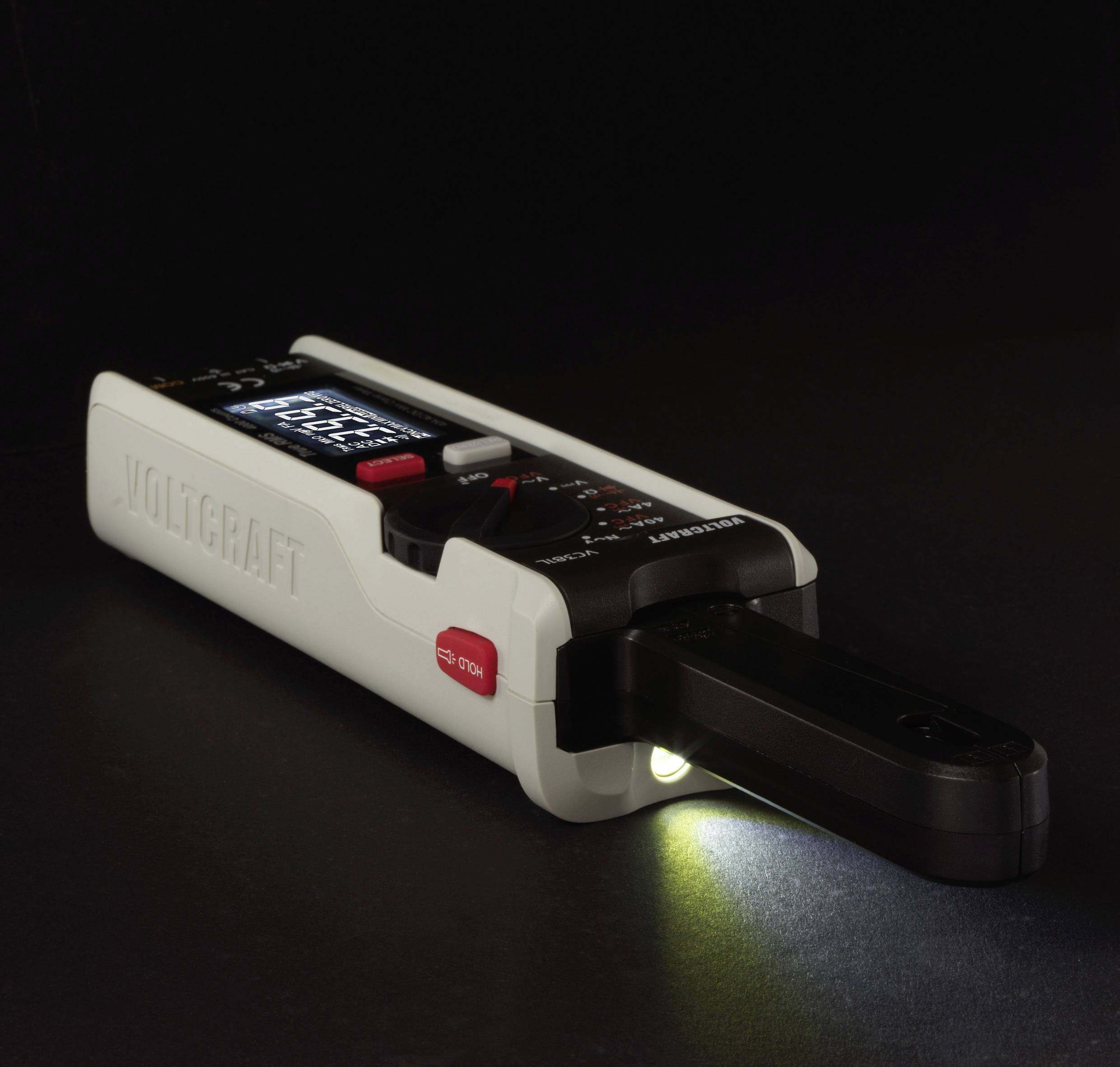 Ein digitales Multimeter in einem dunklen Raum zeigt leuchtende Displayanzeigen. Eine LED-Lampe beleuchtet die rechte Seite.