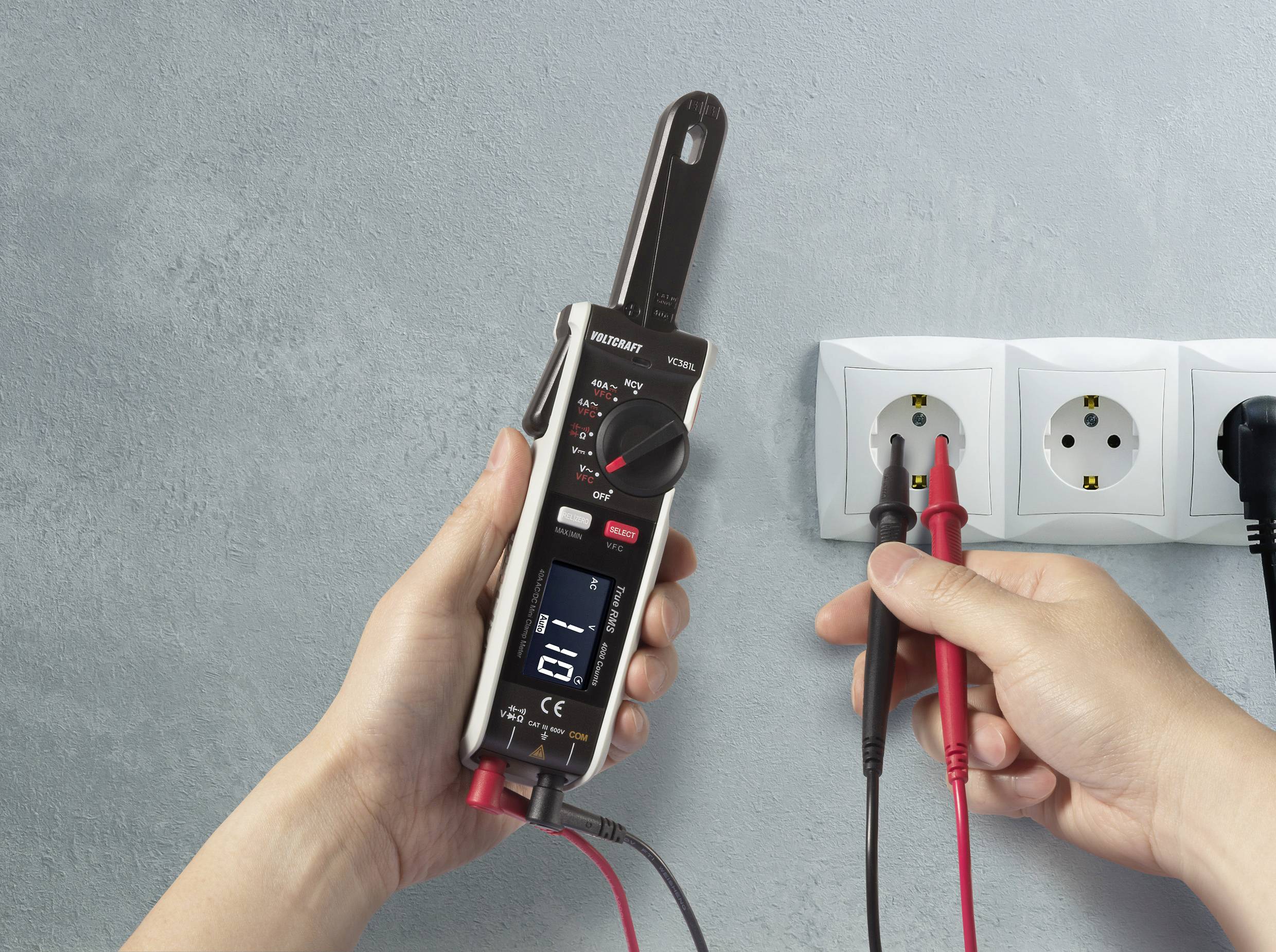 Eine Person verwendet ein digitales Multimeter, um die Spannung in einer Steckdose zu messen. Das Display zeigt Details zur Messung.