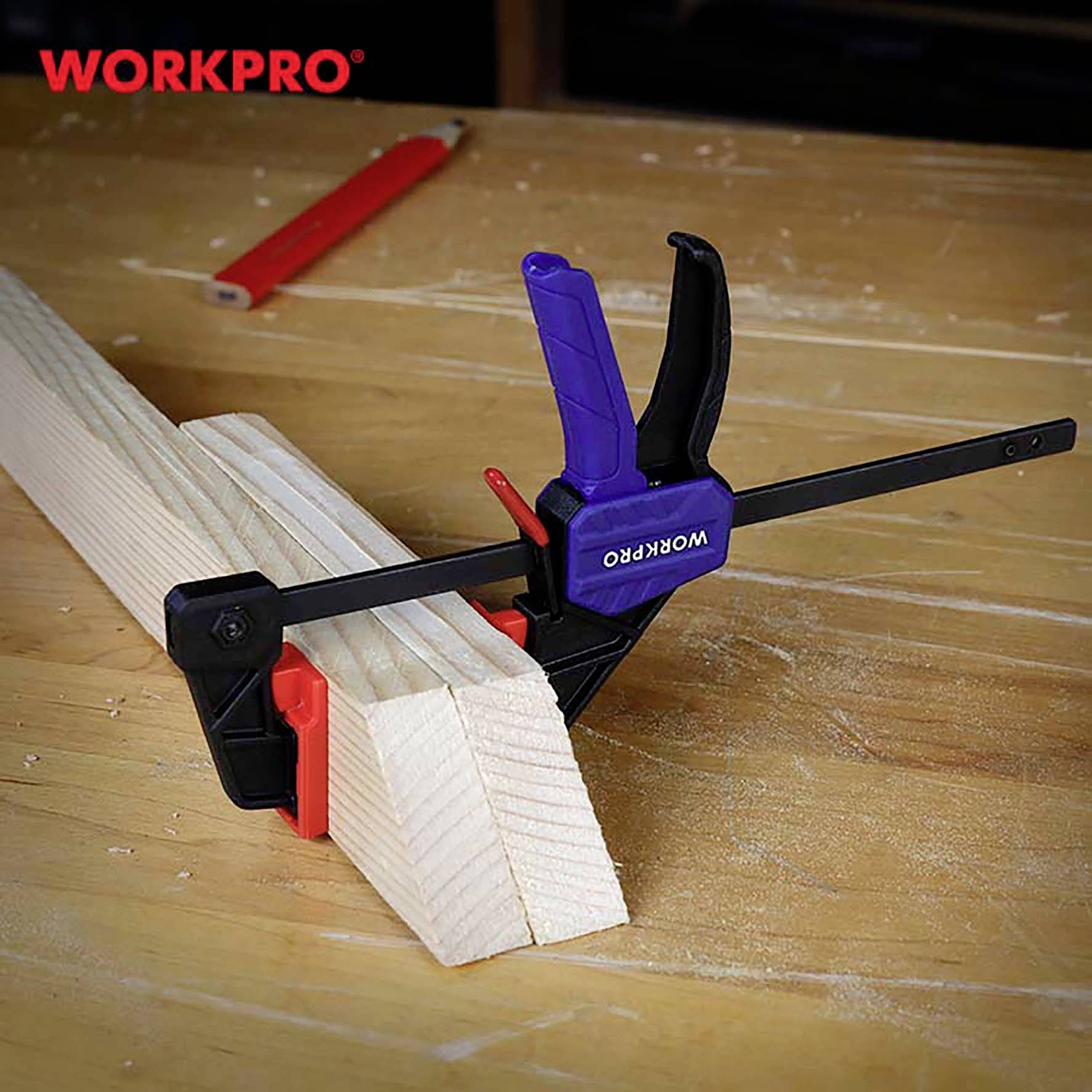 Eine Werkbank mit einem Holzstück, das mit einer blauen und schwarzen Klemme der Marke 'WORKPRO' fixiert ist. Im Hintergrund ein roter Bleistift.