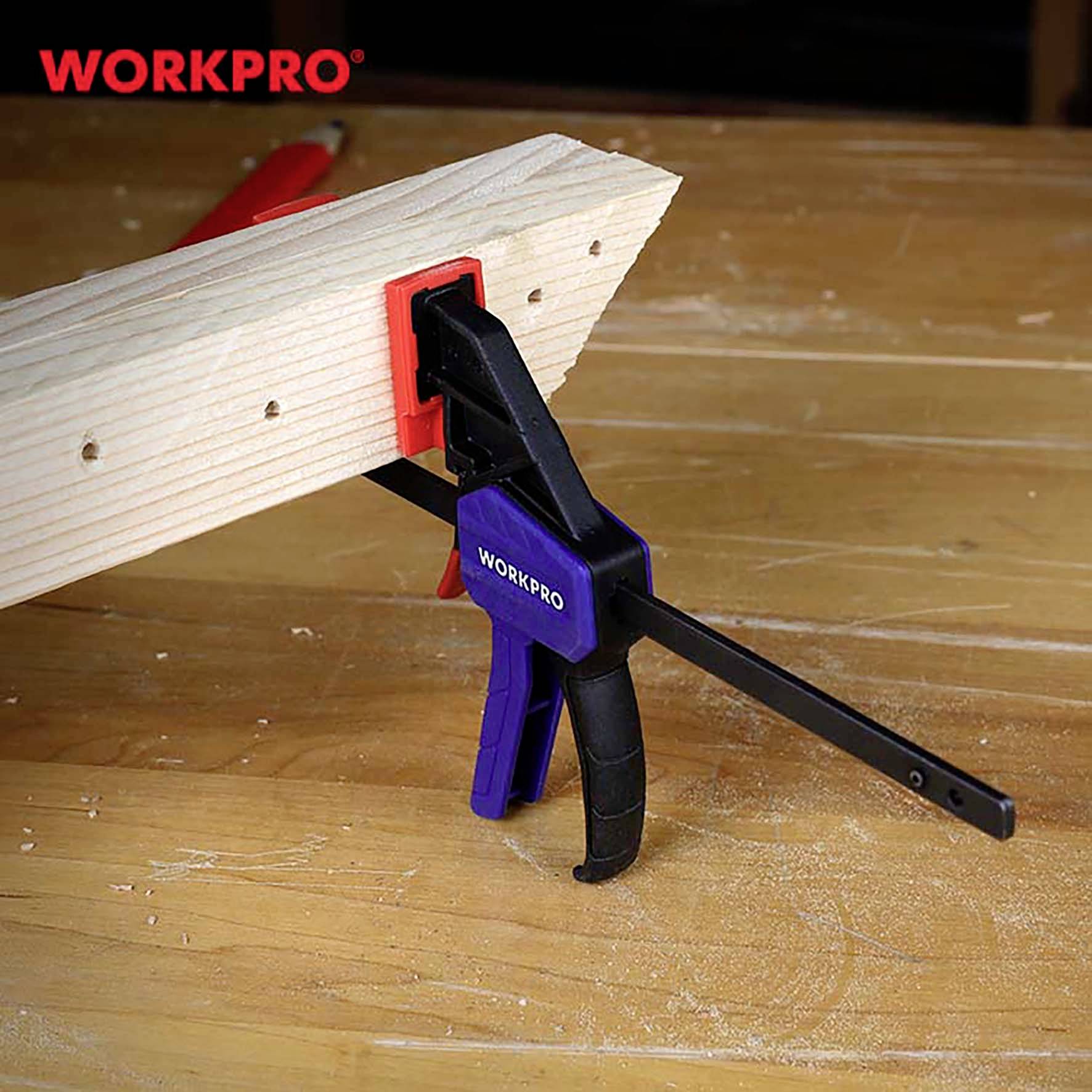 Ein blau-schwarzes Spannwerkzeug hält ein Holzbrett auf einem Tisch. Die Marke 'WORKPRO' ist sowohl auf dem Werkzeug als auch im Bild zu sehen.