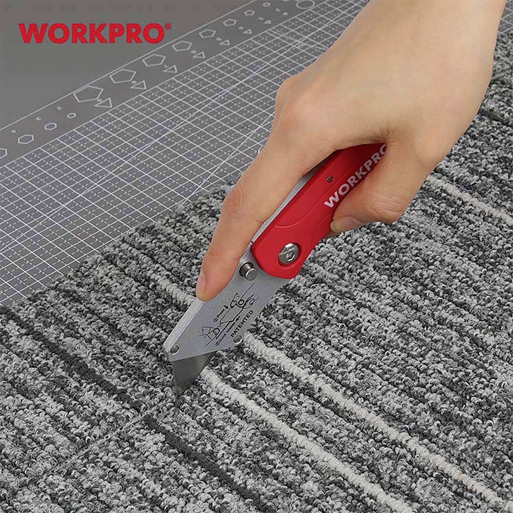 Eine Hand schneidet mit einem WORKPRO Teppichmesser einen grauen Teppich auf einer Schneidematte mit Rastermuster.