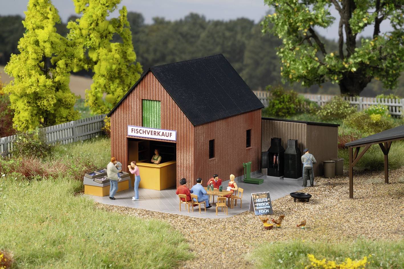 Ein Modell eines Fischverkaufsladens in ländlicher Umgebung, mit Figuren, die Fisch kaufen und eine Tafel mit der Aufschrift 'Frisch geräuchert heute'.