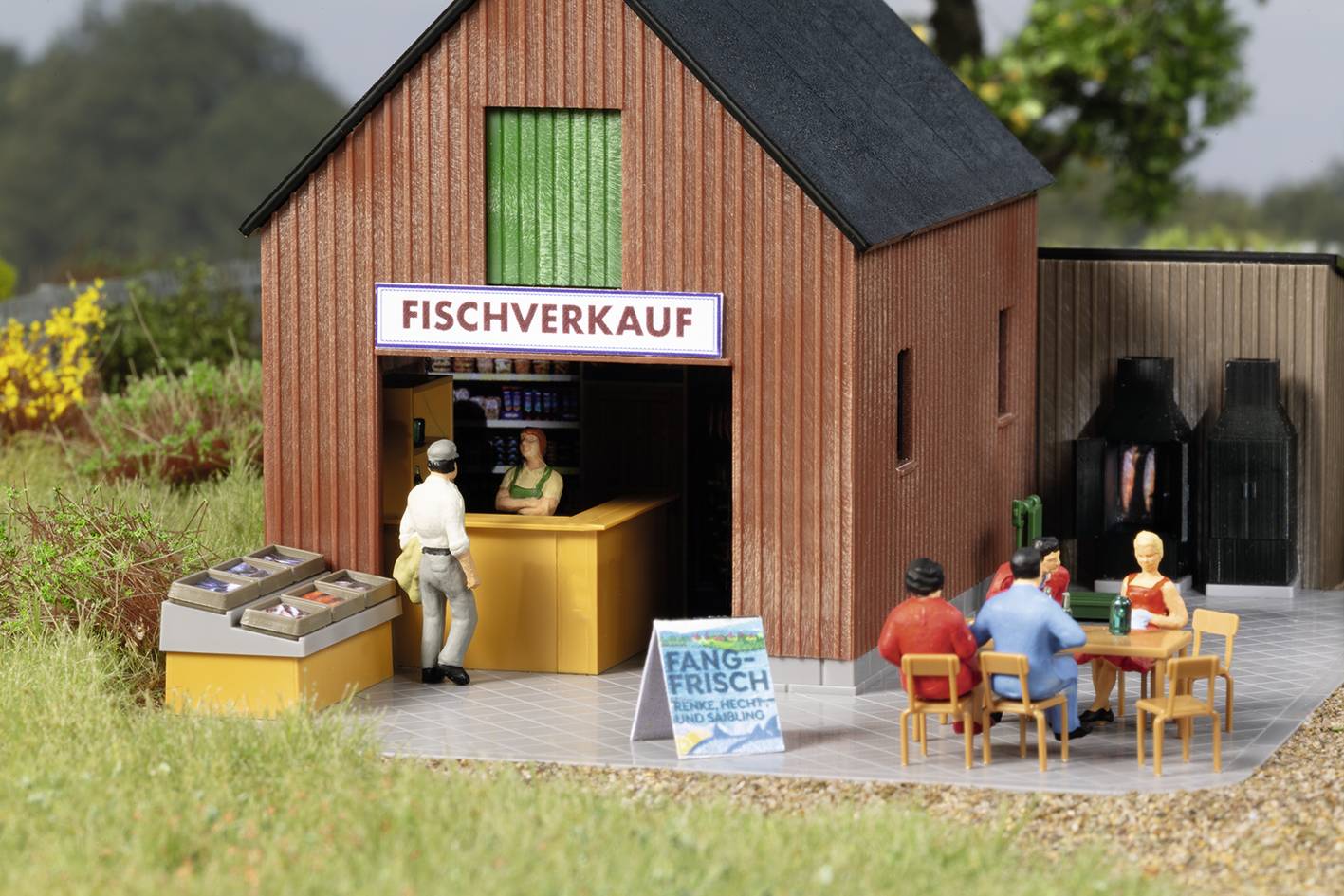 Ein Mann kauft an einem Fischverkaufsstand ein, daneben sitzen drei Menschen an einem Tisch. Ein Schild zeigt 'Fangfrisch'.